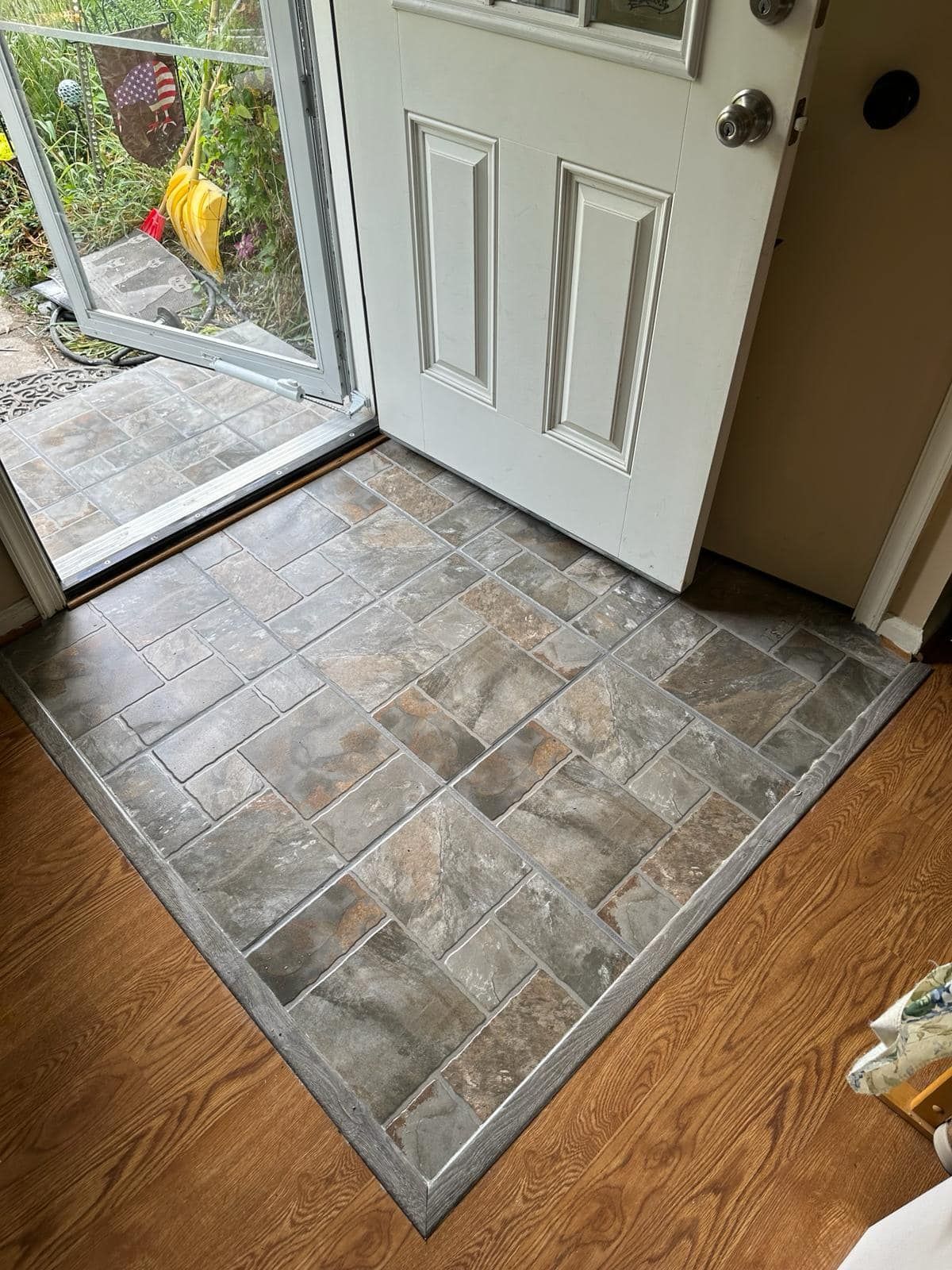 Doorway with tiled entry rug; white door, wooden floor, and screen door.