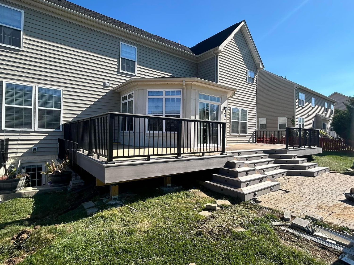 Backyard deck with black railing and steps leading to a house with siding and windows.