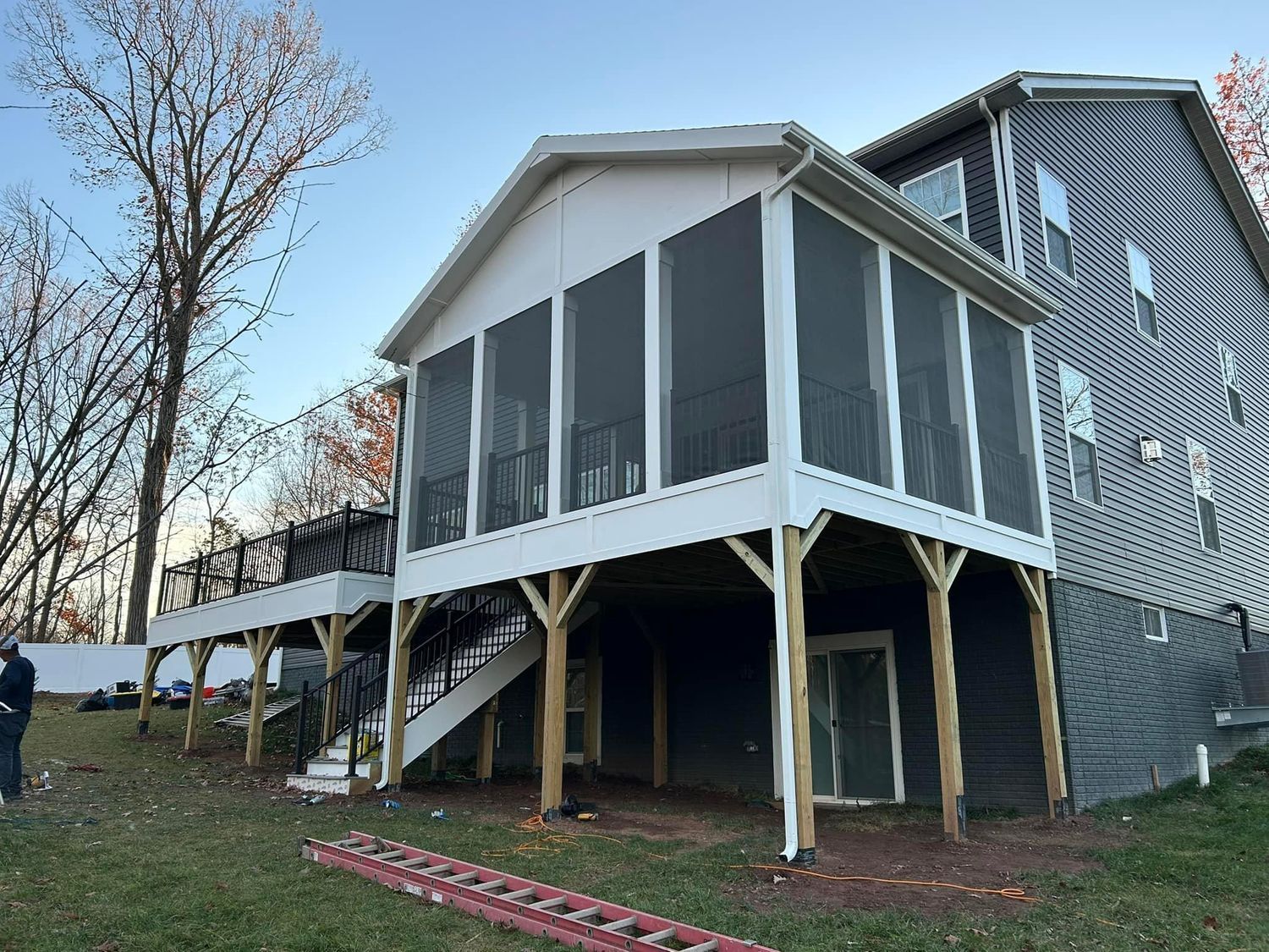 Screened-in porch with white trim, stairs, and black screens attached to a two-story house.