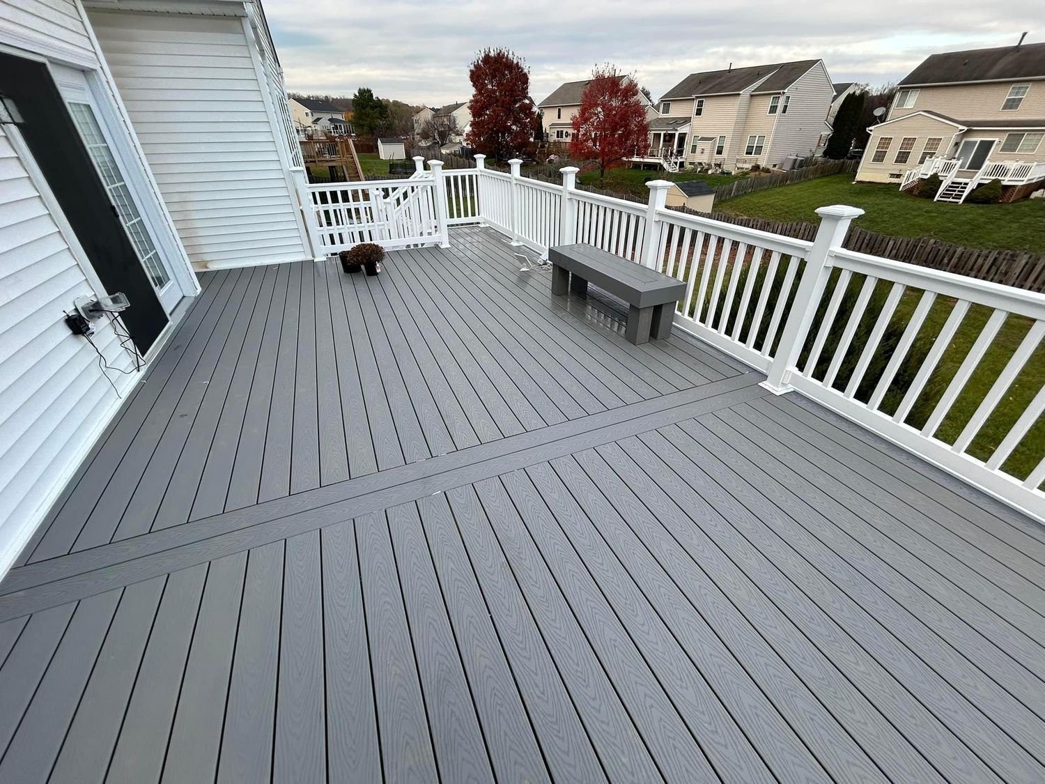 Gray composite deck with white railing, a gray bench, and a dog outdoors.
