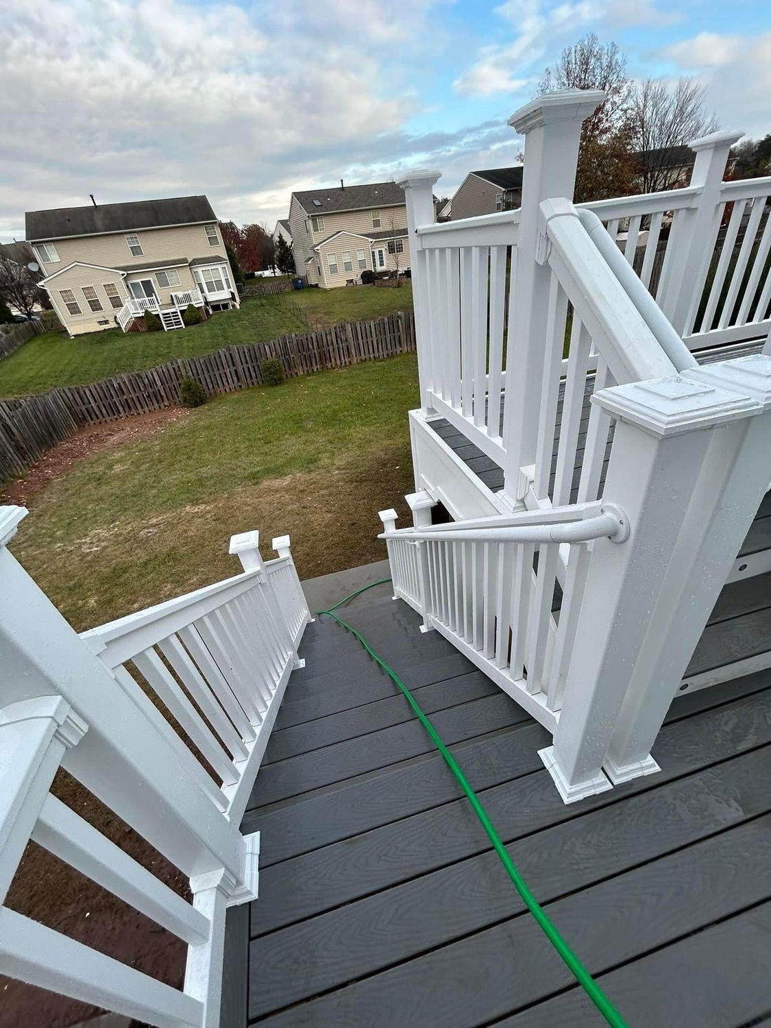 White deck with gray steps, overlooking a grassy yard and houses under a cloudy sky.