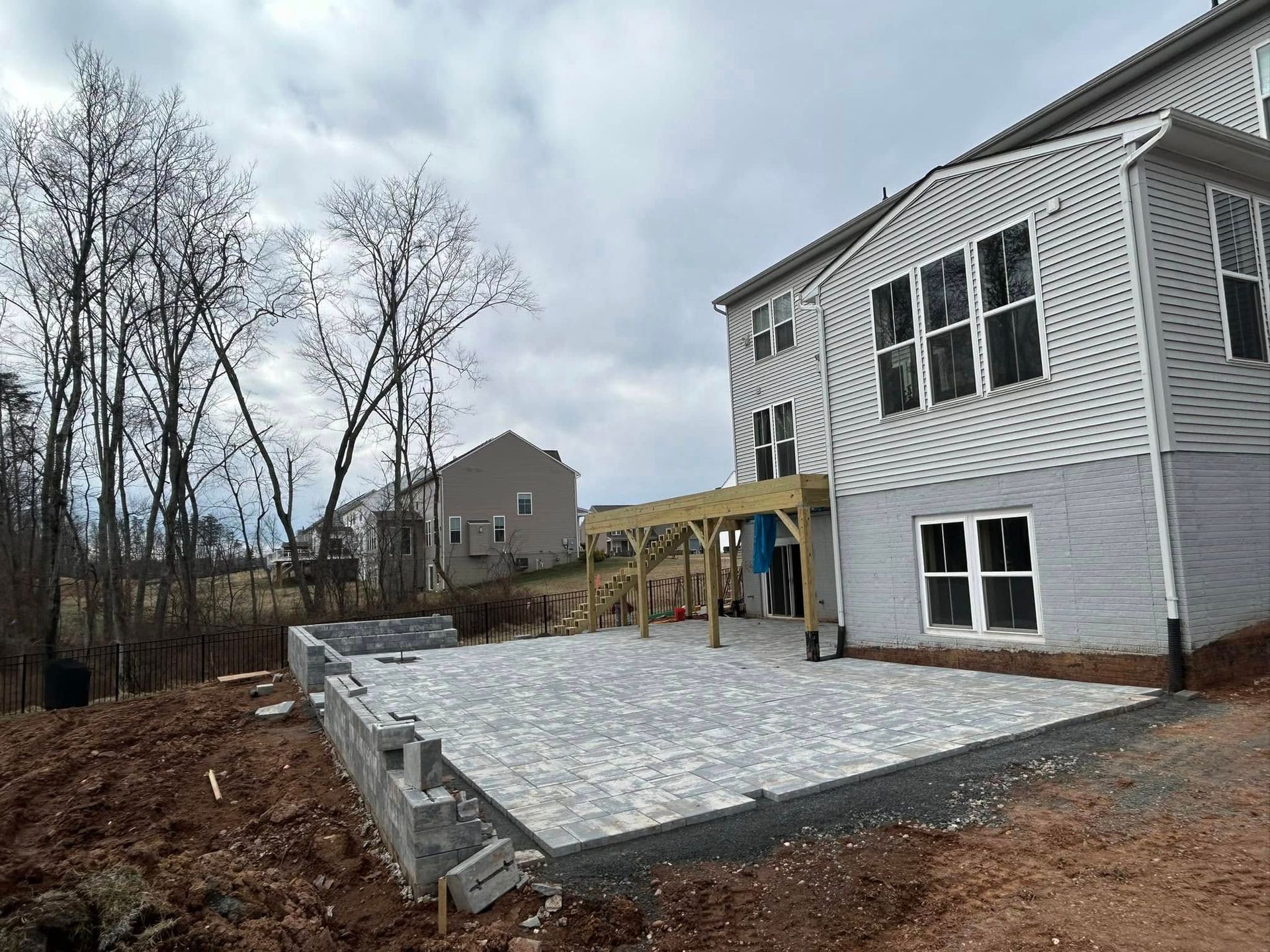 Backyard patio under construction with a partially built pergola, next to a house. Cloudy sky.