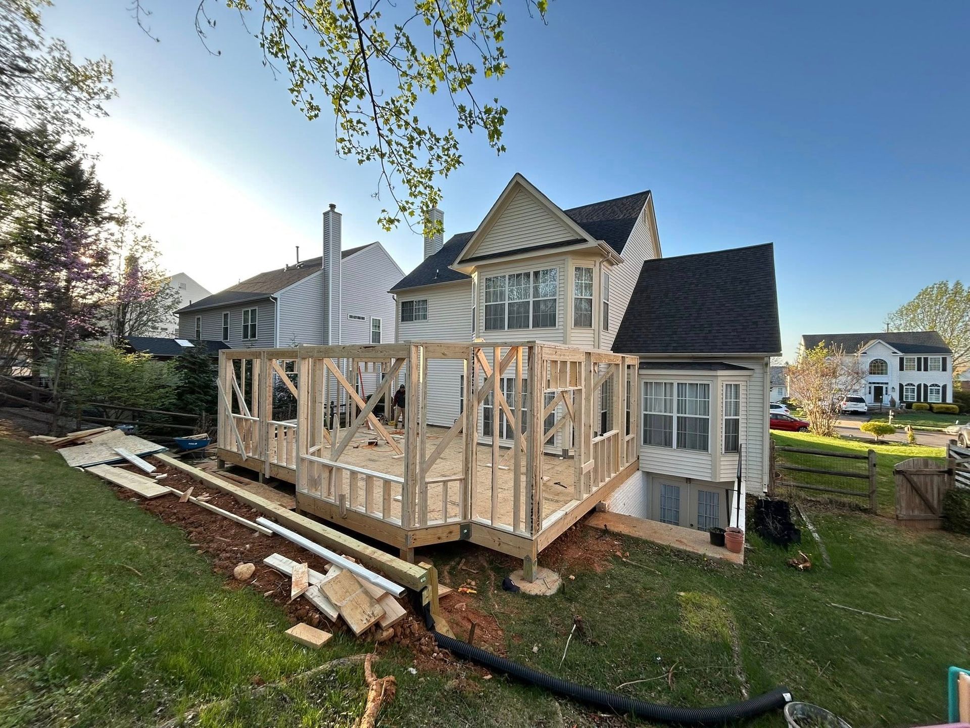 Wooden deck under construction next to a two-story house; sunny day.