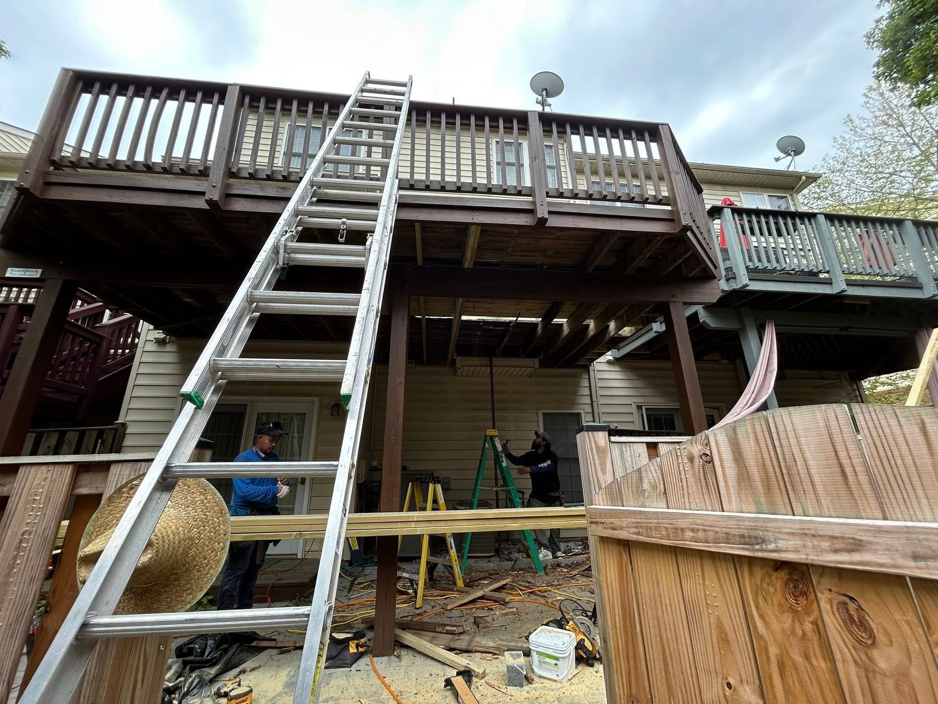 Workers repairing a two-story wooden deck with a ladder. Sunny day.