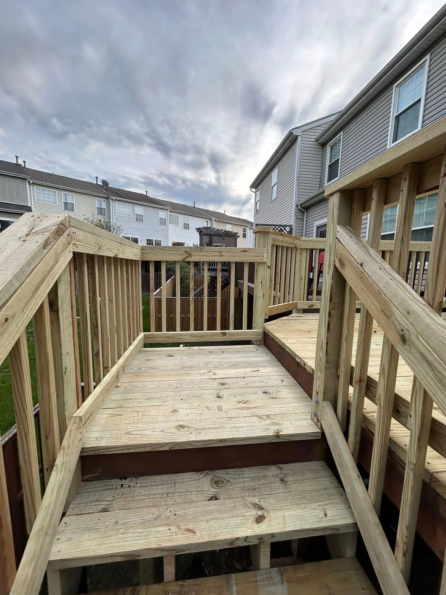 Wooden deck with stairs and railings, leading toward a backyard, cloudy sky overhead.