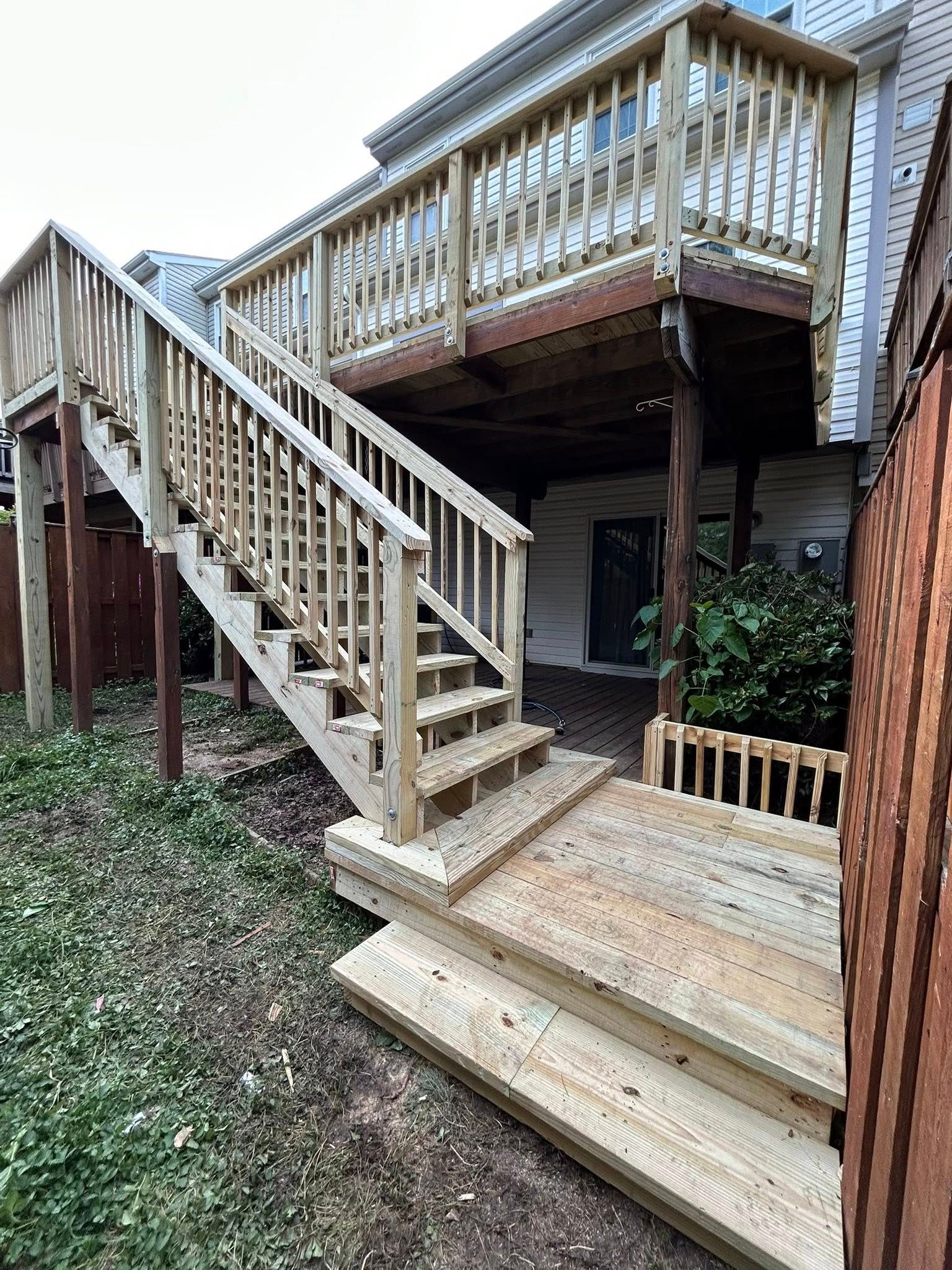 Wooden deck and stairs leading up to a house, built in a backyard, surrounded by greenery.
