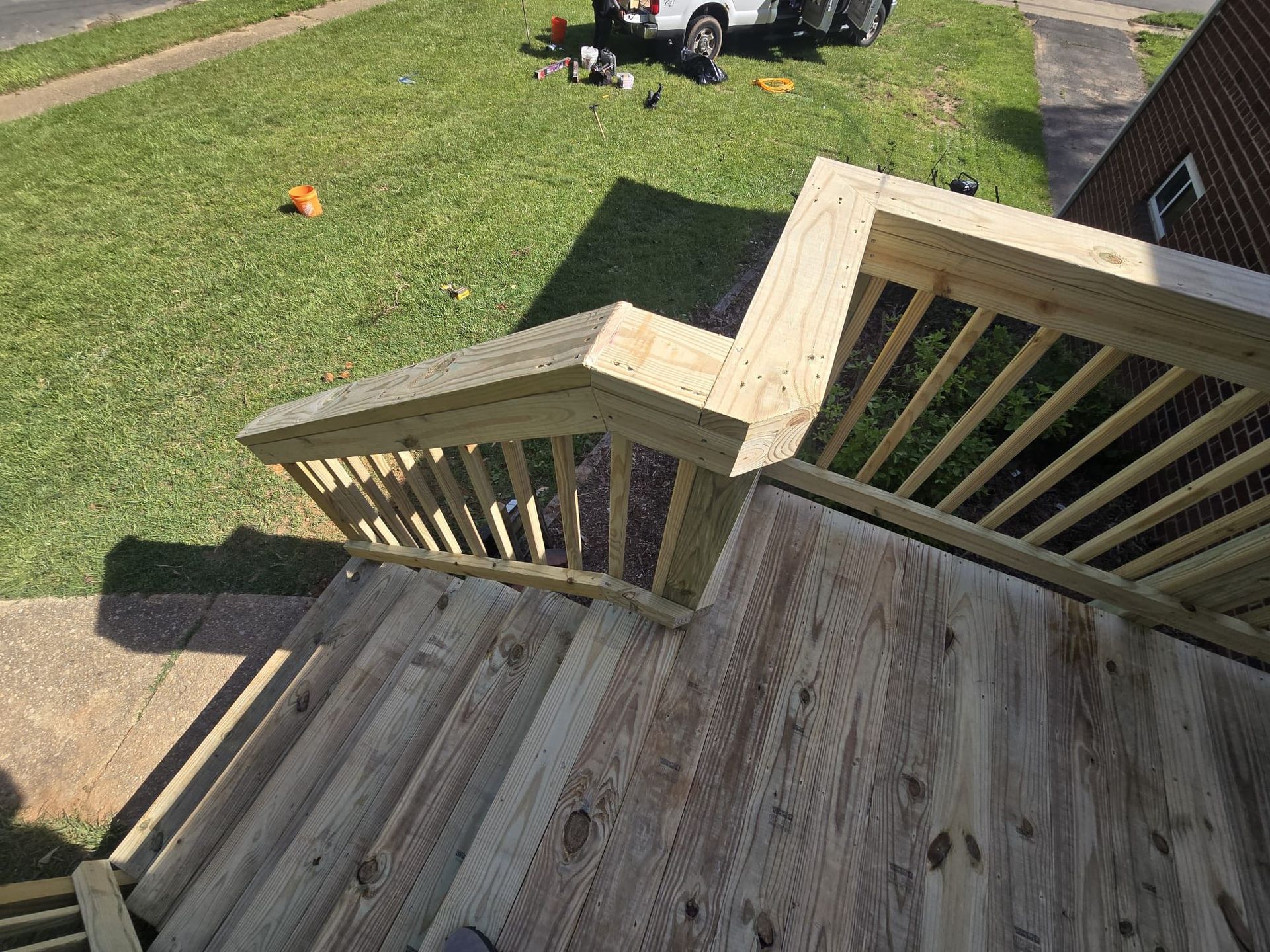 Wooden deck with railing and steps leading down to green grass. A truck is visible in the background.