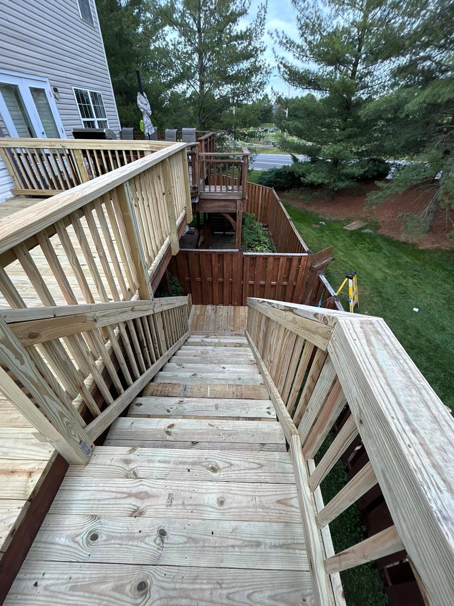 Wooden staircase leading down from a deck, with railings, to a fenced yard.