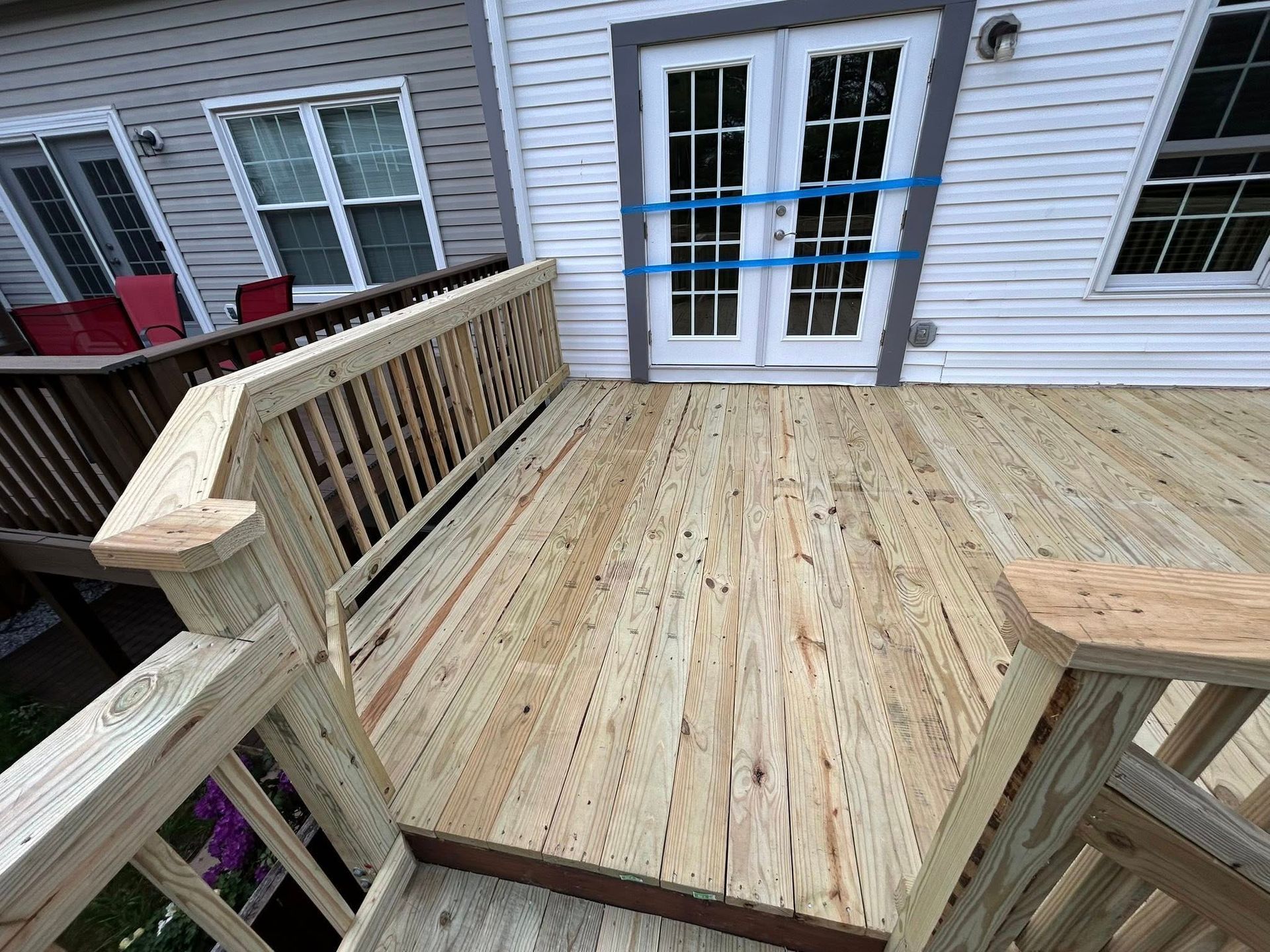 Wooden deck with railing leading to white French doors. Blue tape on doors.