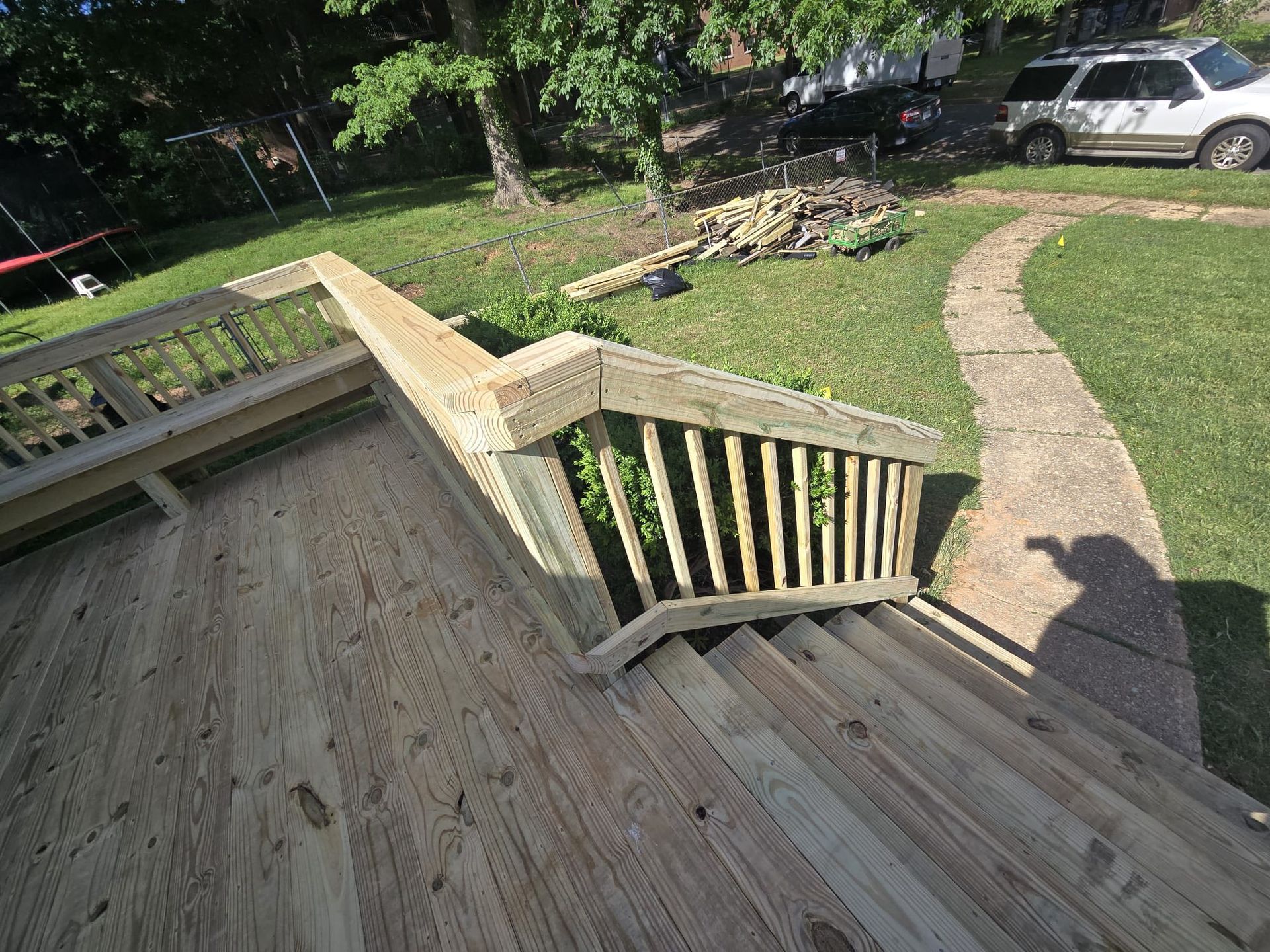 Wooden deck with stairs leading to a grassy yard, stone pathway, and parked car.