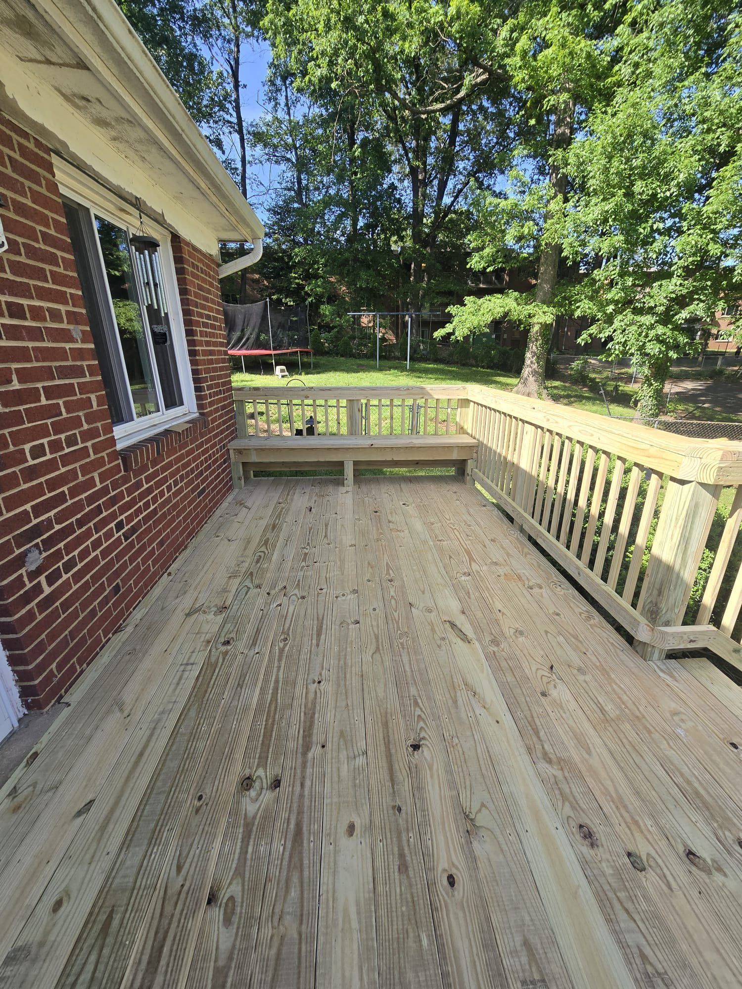 Wooden deck attached to a brick building, with railing and a built-in bench.