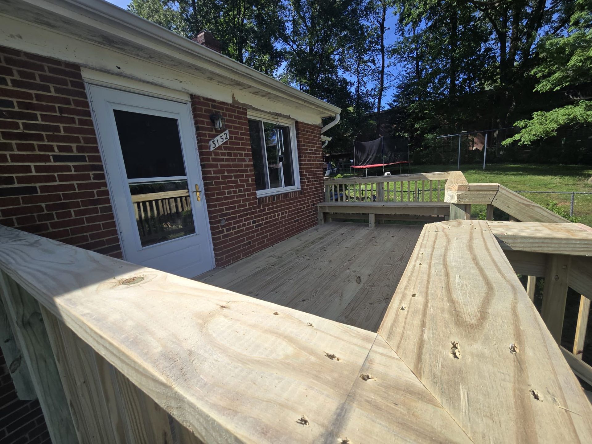 Wooden deck attached to a brick house; light wood railing; sunny outdoor setting.