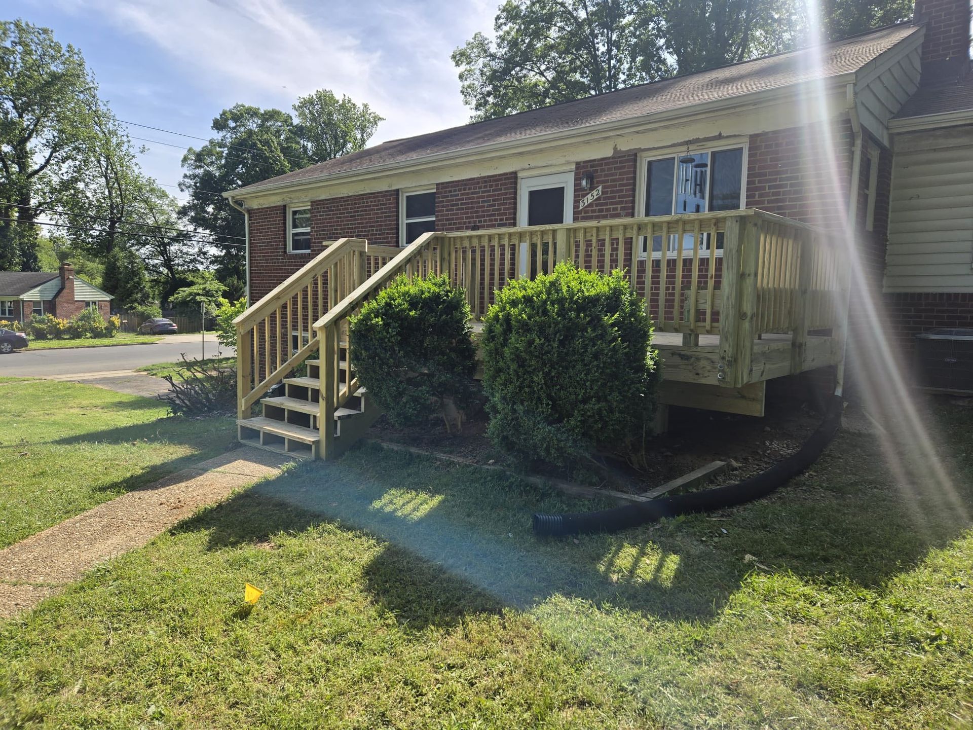 Wooden deck and stairs leading to a brick house with green shrubbery in the yard.