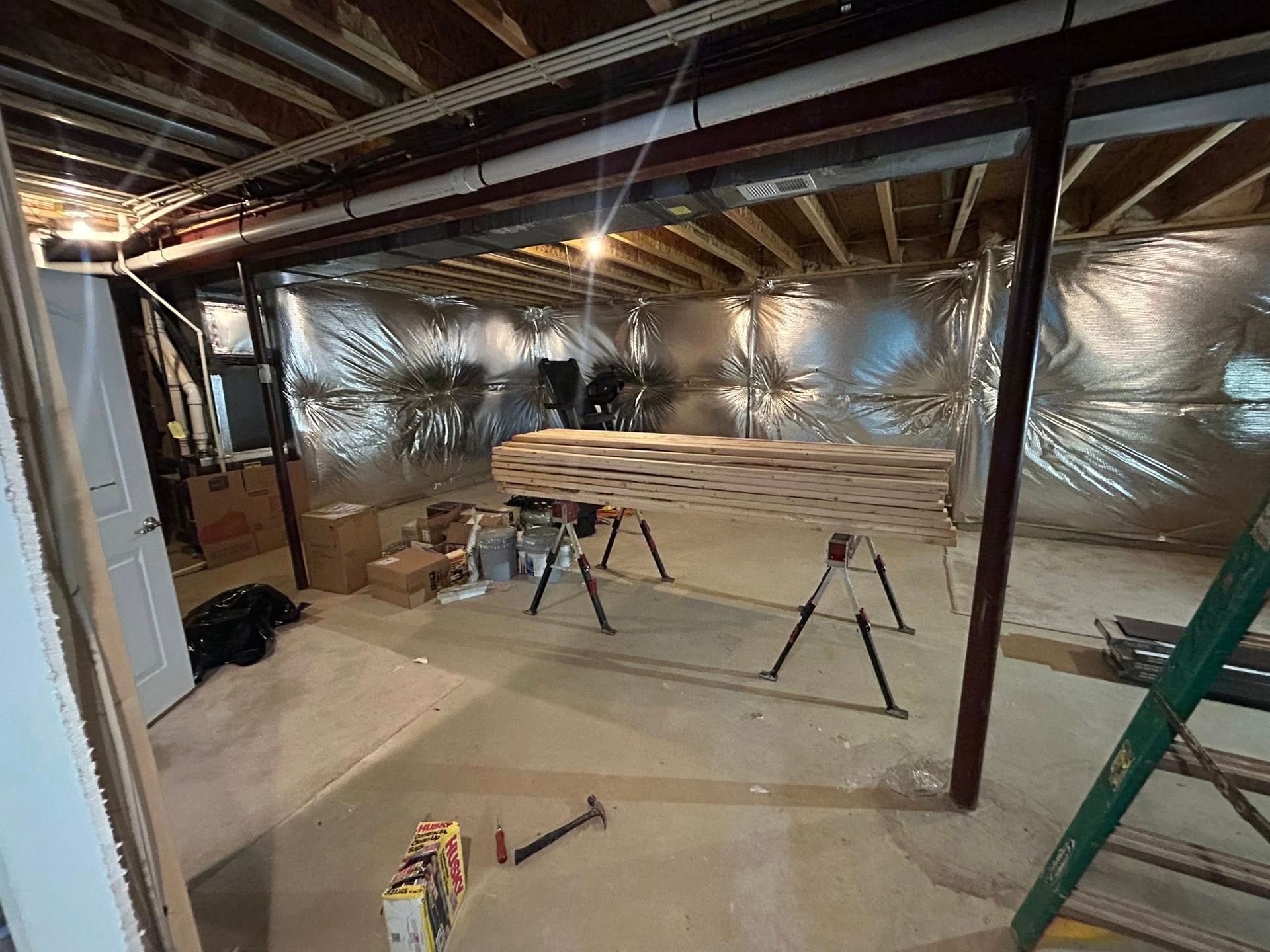 Basement construction in progress: wood on sawhorses, insulation, support beams.