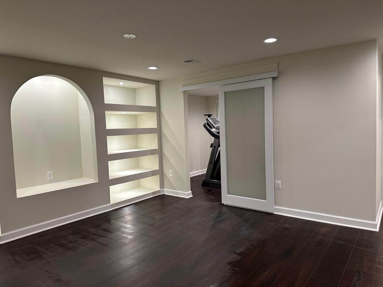 Empty room with dark wood floor, built-in shelves, arched niche, and sliding frosted glass door.
