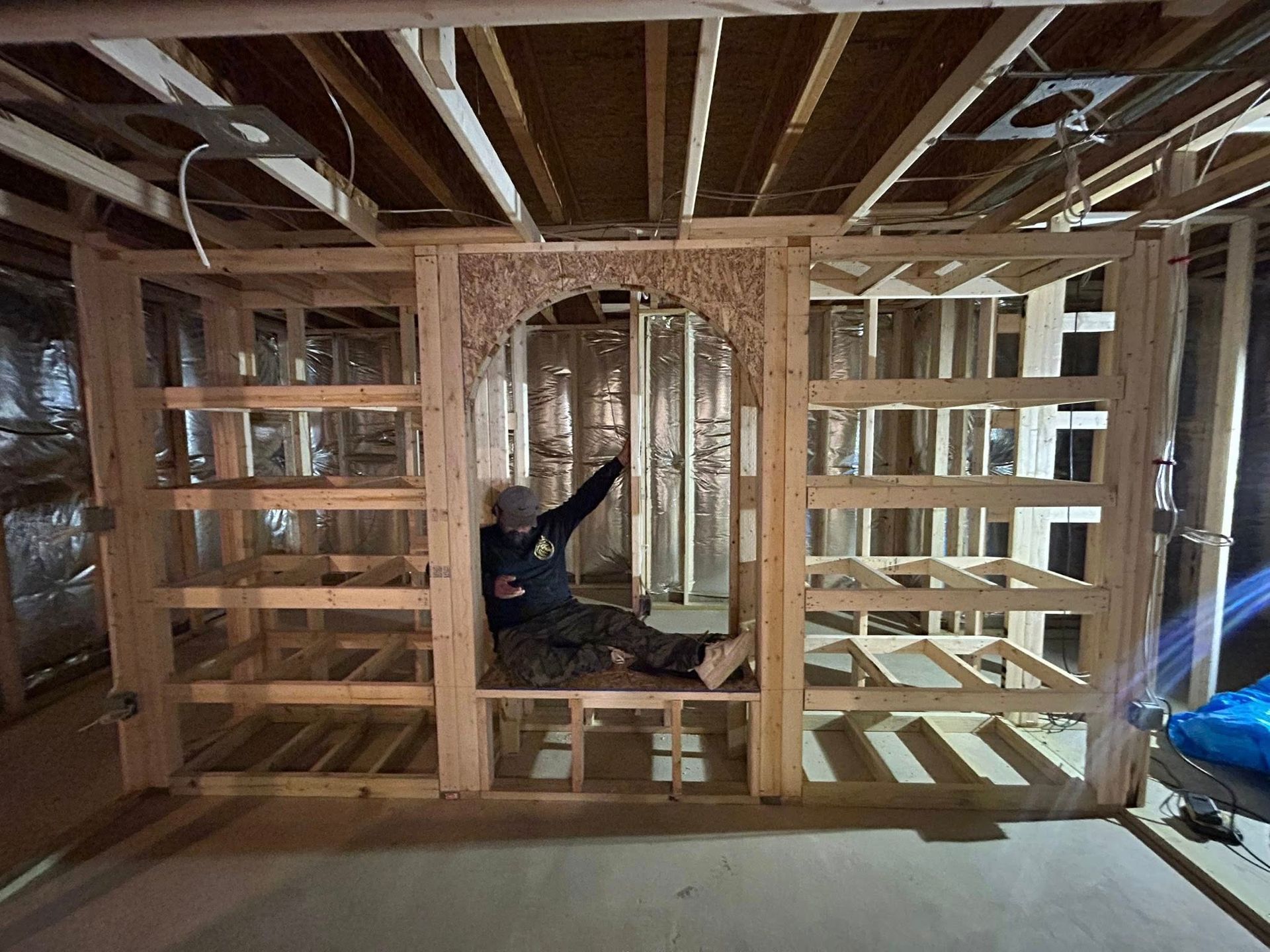 Man in a wooden framed alcove with shelving in an unfinished basement. He is pointing upward.