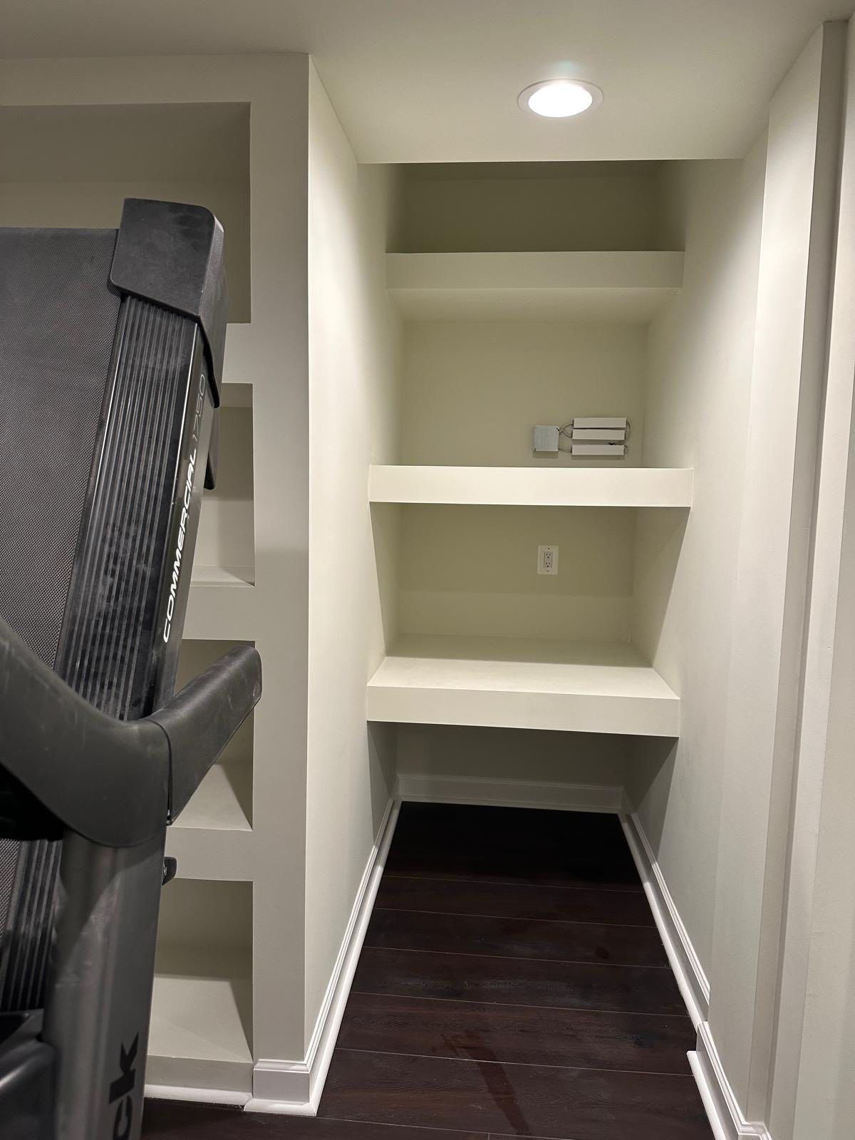 Treadmill next to built-in shelves in a room with dark flooring and light-colored walls.