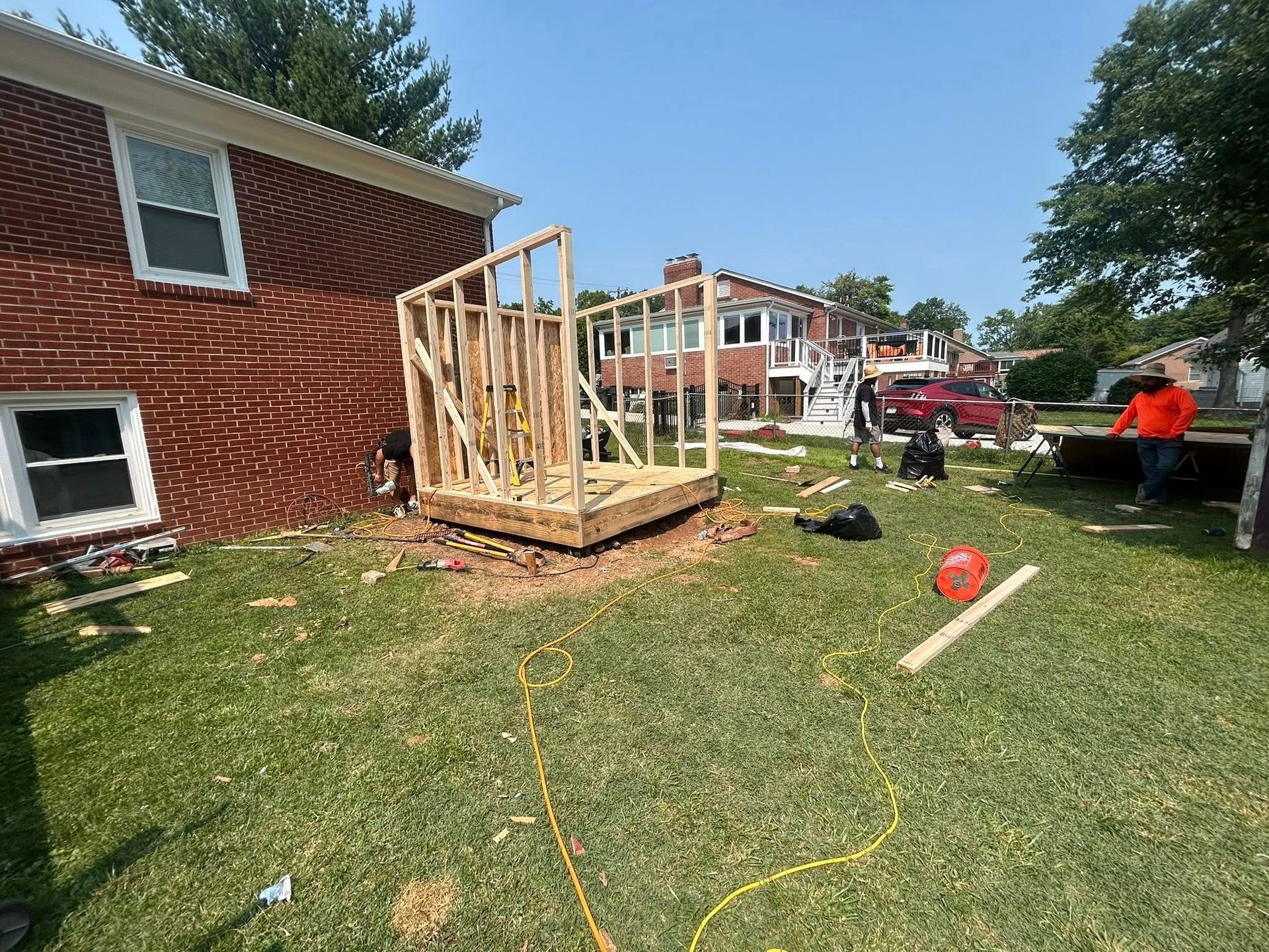 Construction of a wooden structure in a grassy backyard next to a brick house.