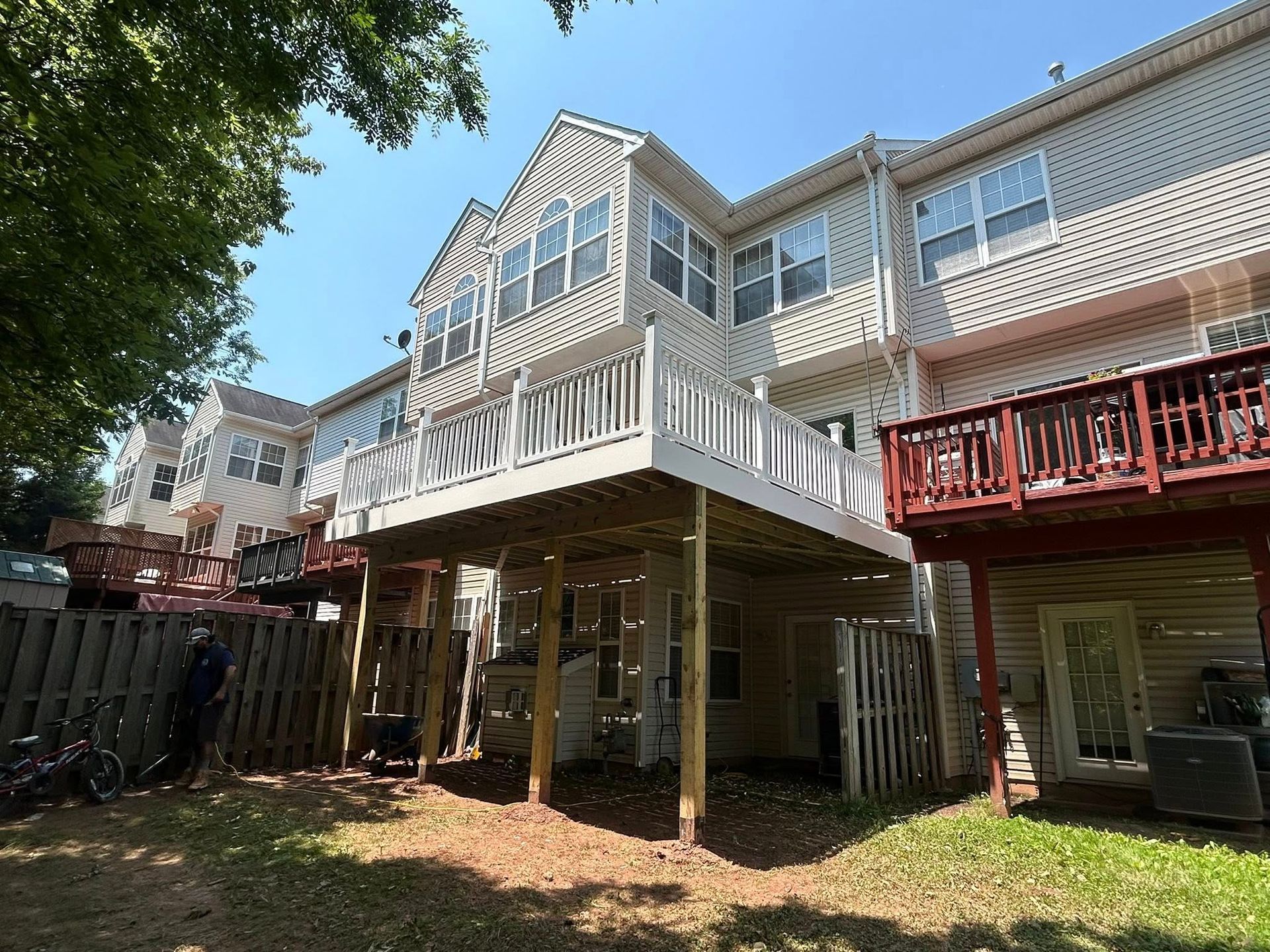 Multi-story townhouses with decks; one deck is freshly painted white. Sunny backyard setting.