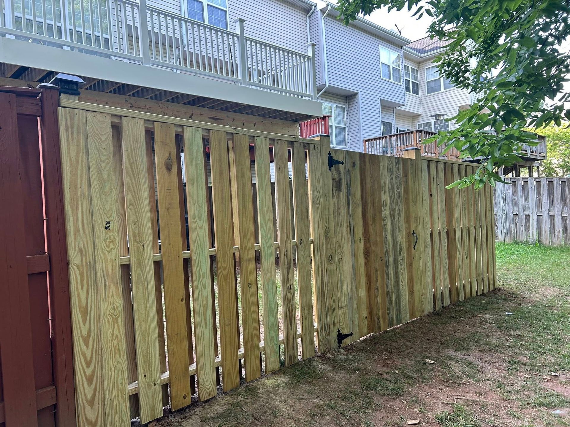 Wooden fence in a backyard next to a deck and house. Green grass and another fence are also visible.
