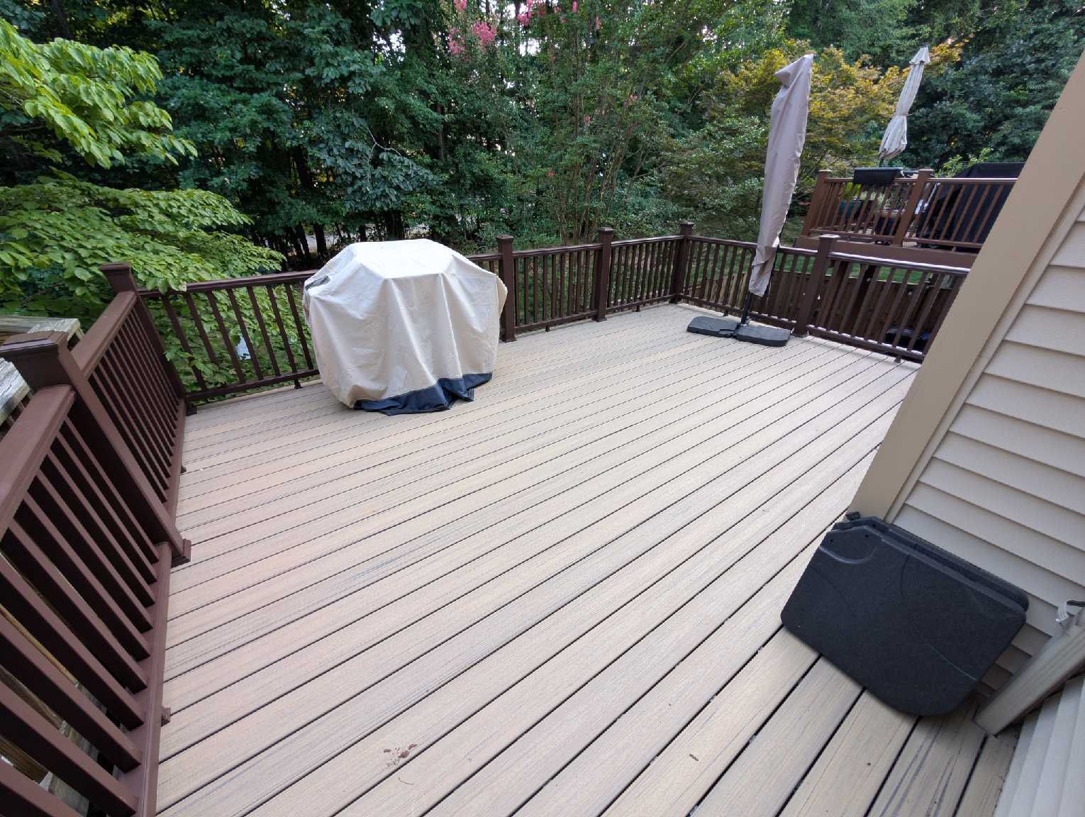 A multi-level wooden deck with a covered grill and umbrella, surrounded by trees.