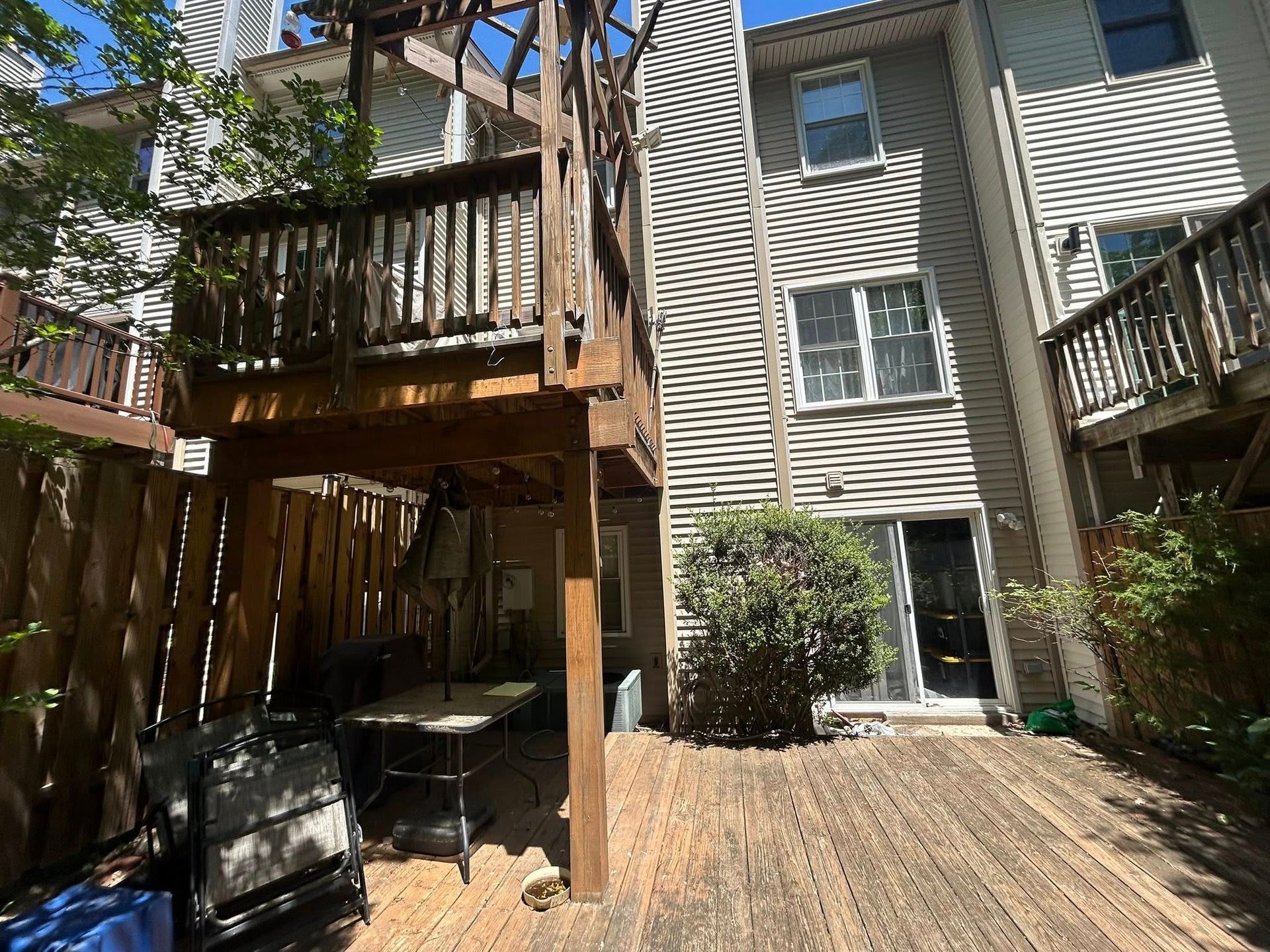 Backyard with wooden deck, two-story building, table, chairs, and greenery.