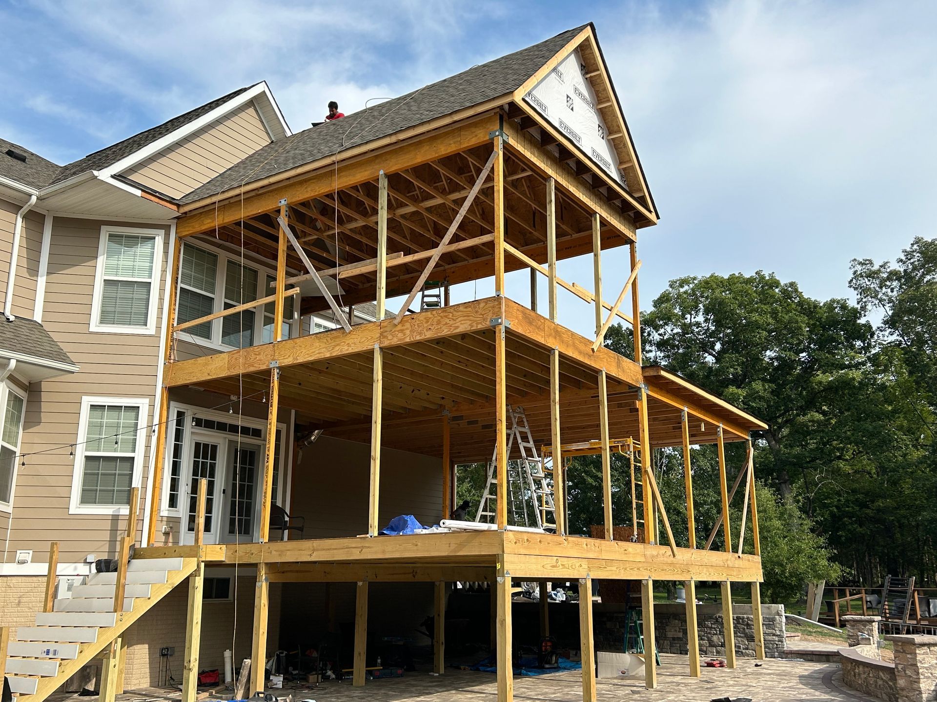 Two-story wooden porch under construction attached to a beige house.