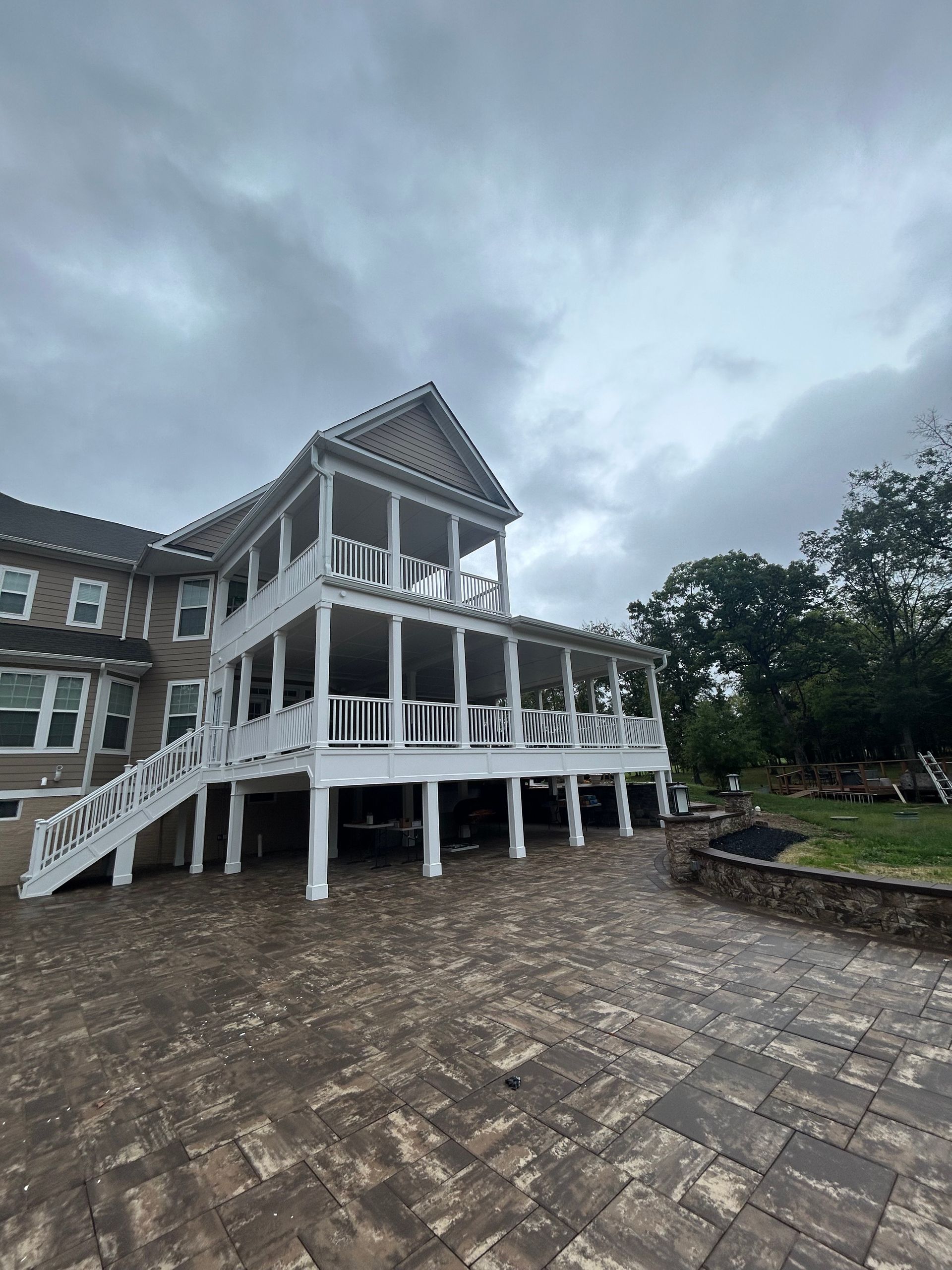 Two-story white porch on a large brick patio, against a cloudy sky.