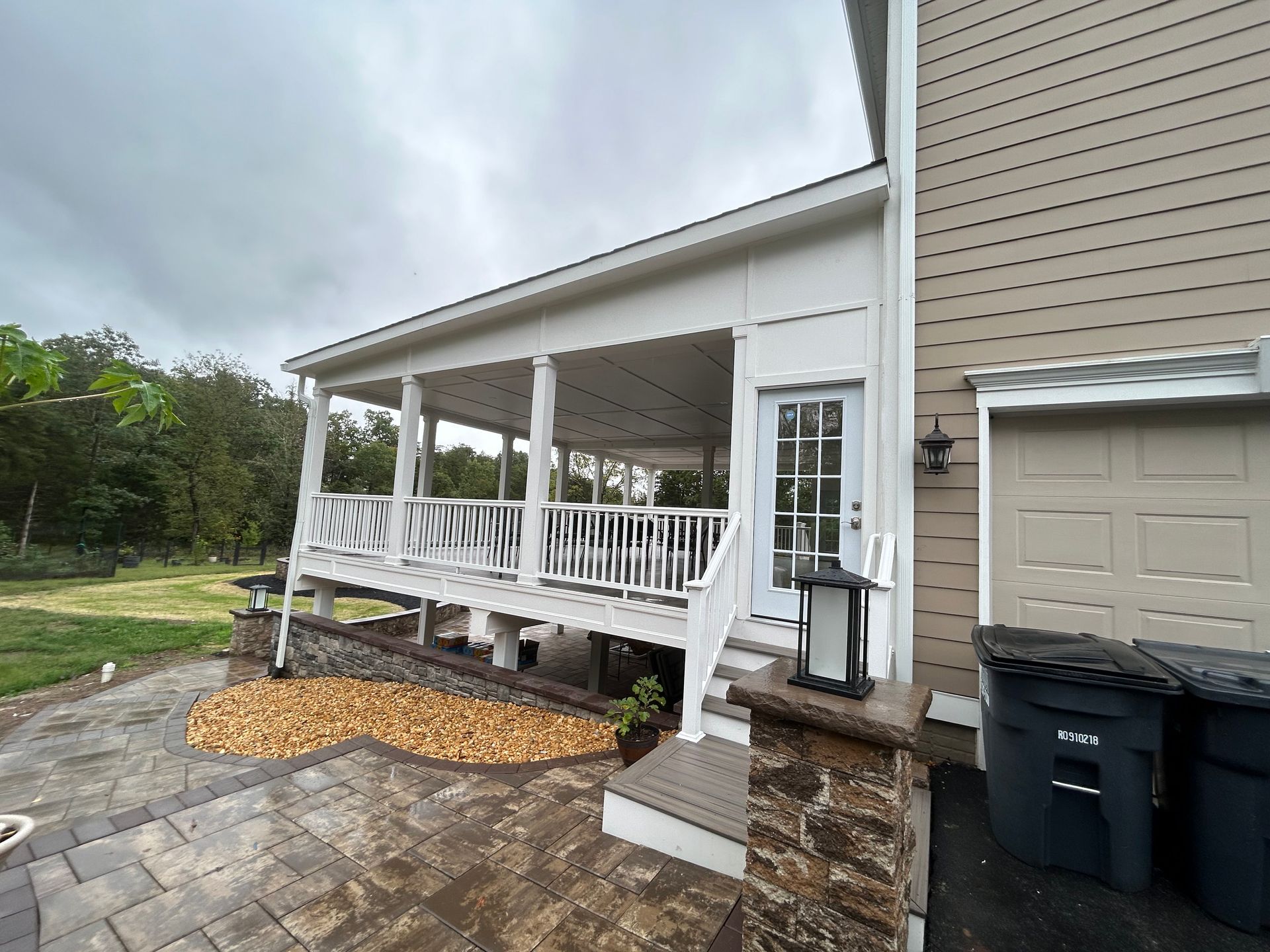 Covered porch with white railing and steps, next to a beige house and garage.