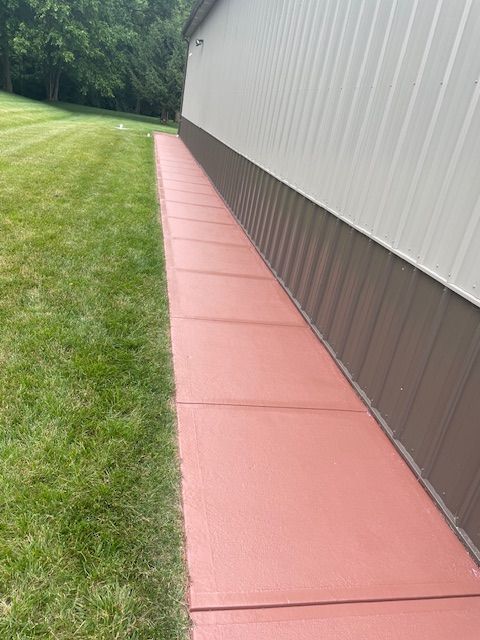 A red sidewalk next to a building and a lush green field.
