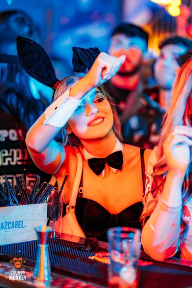 A woman dressed as a playboy bunny is sitting at a bar.