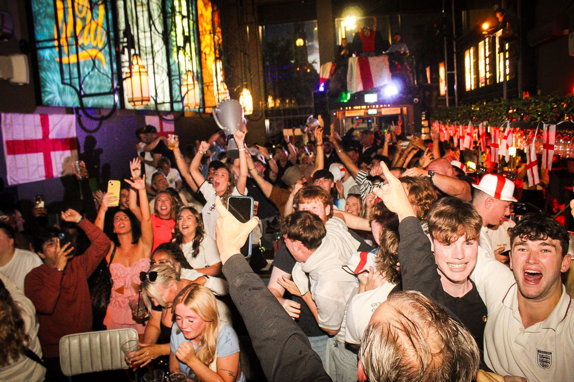 A crowd of people are standing in a room with their arms in the air.
