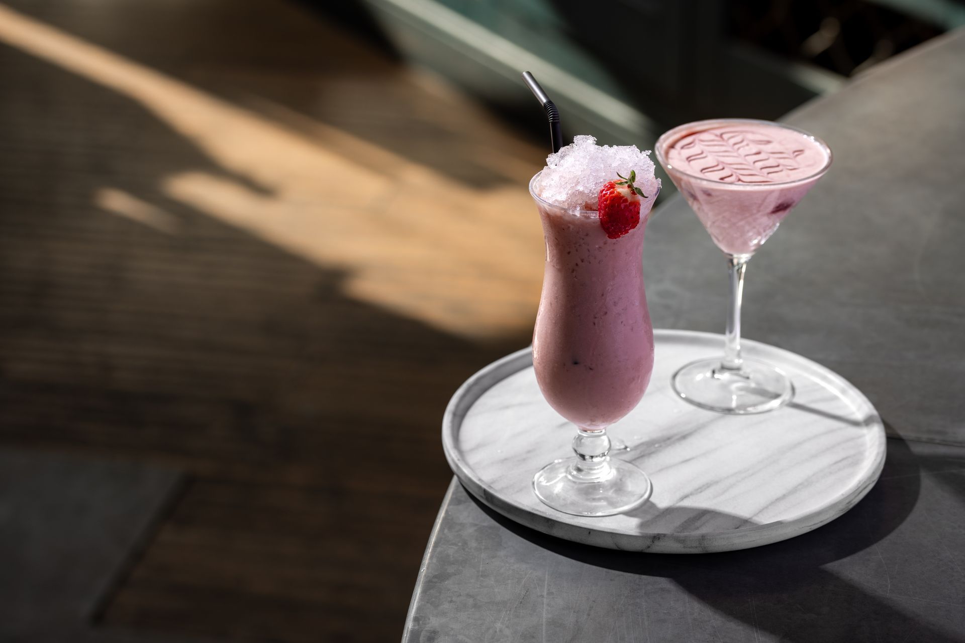 Two pink drinks are sitting on a marble tray on a table.
