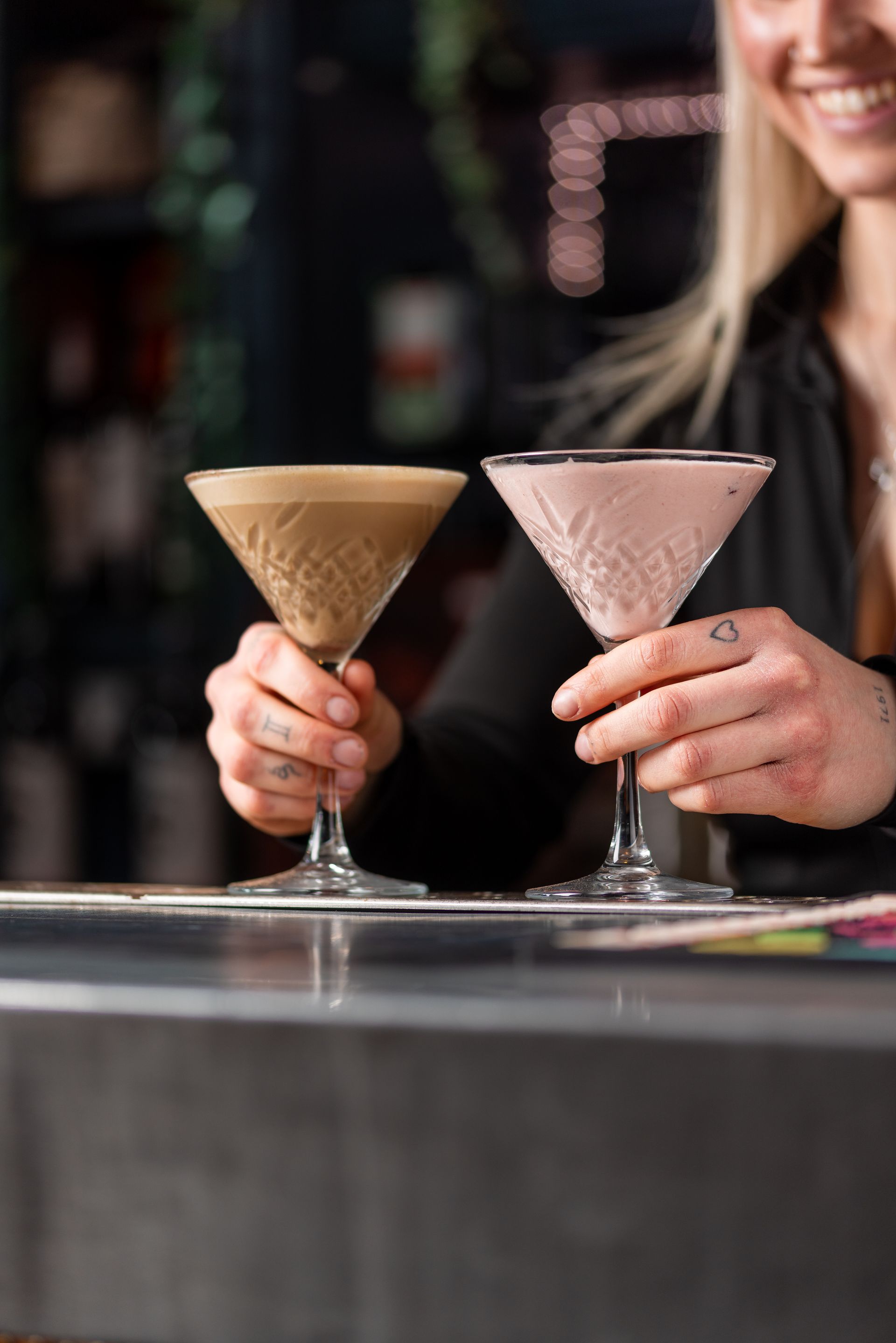 A woman is holding two martini glasses at a bar.