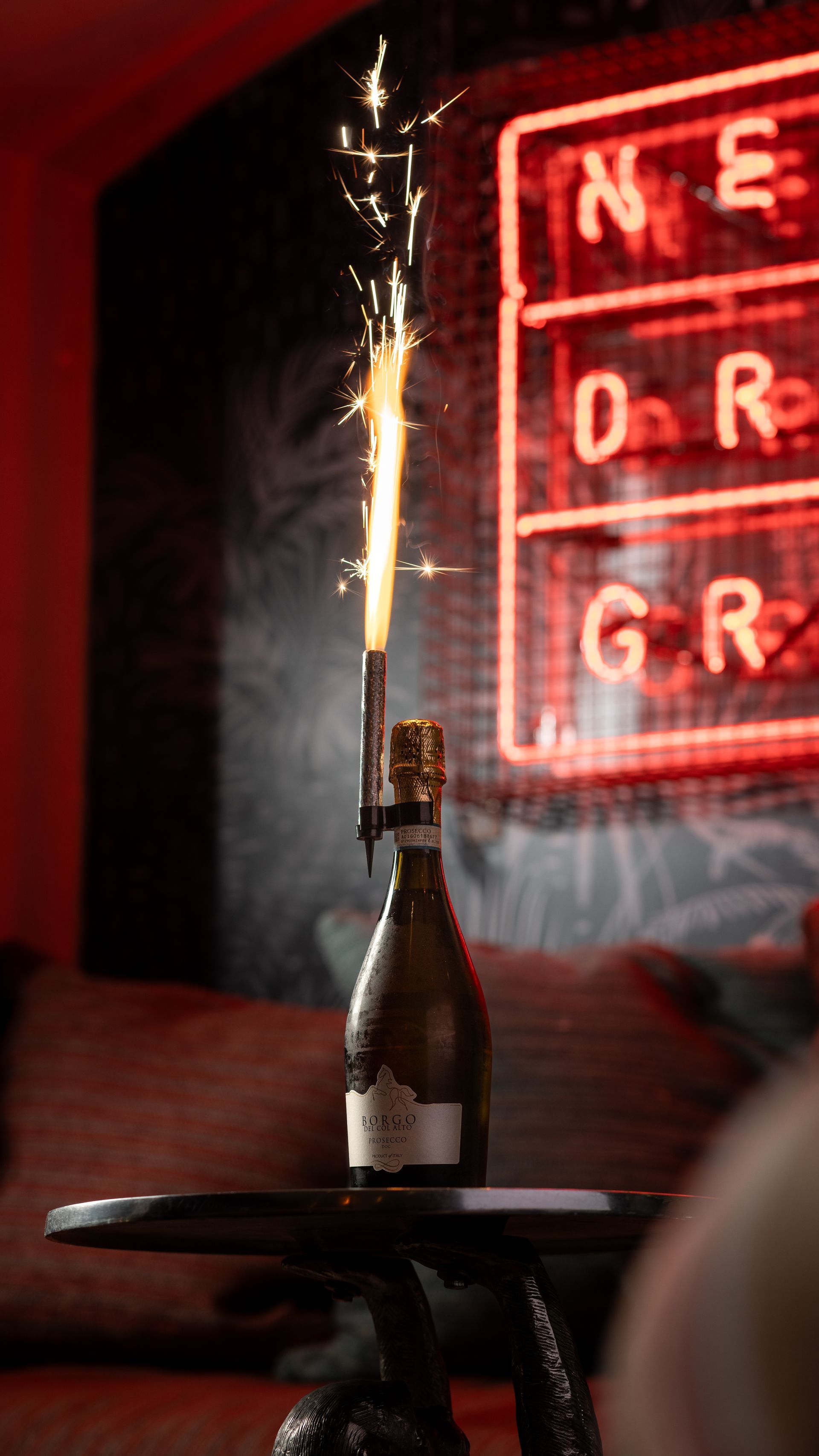 A bottle of champagne with sparklers coming out of it is on a table.