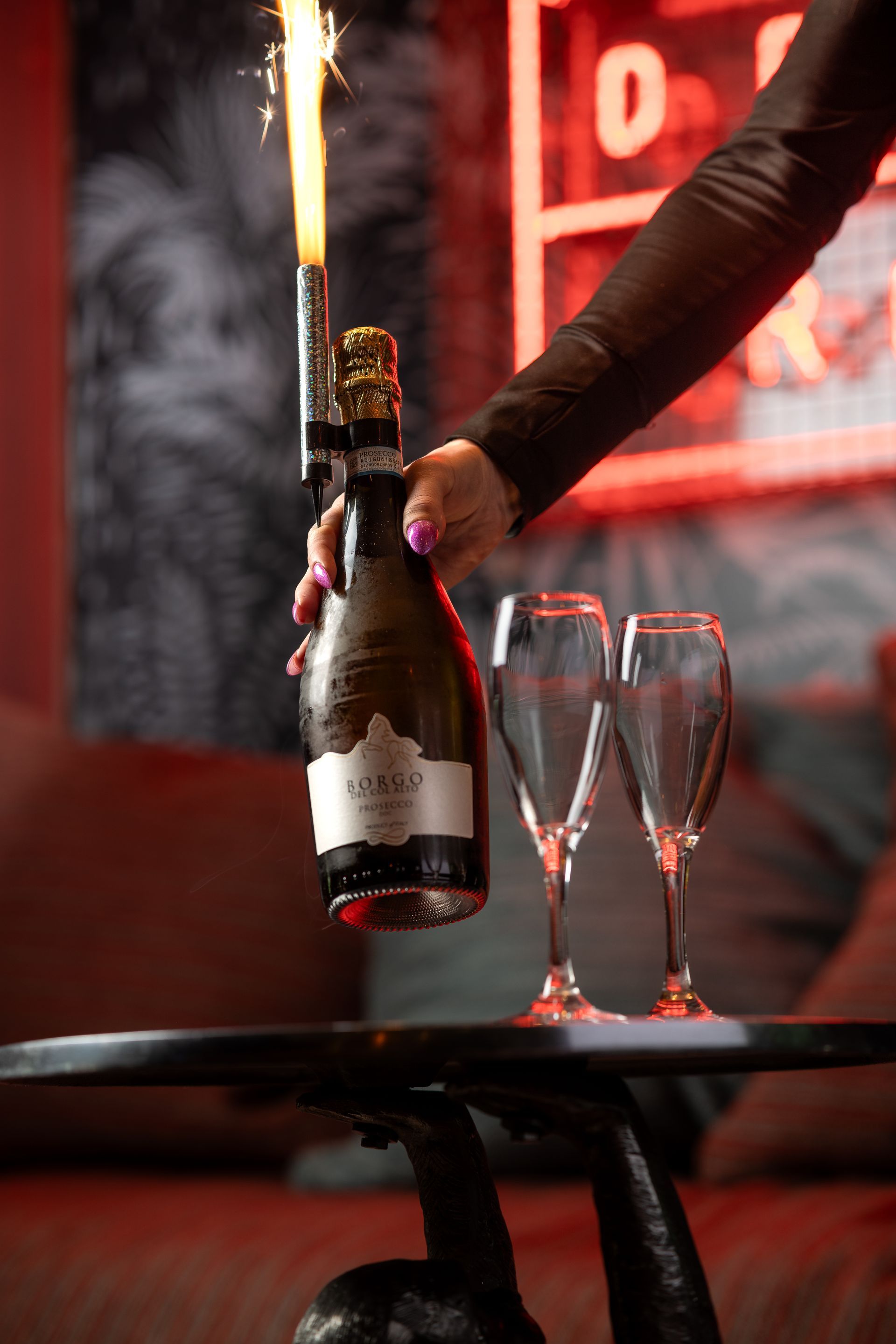 A woman is pouring champagne into two glasses on a table.