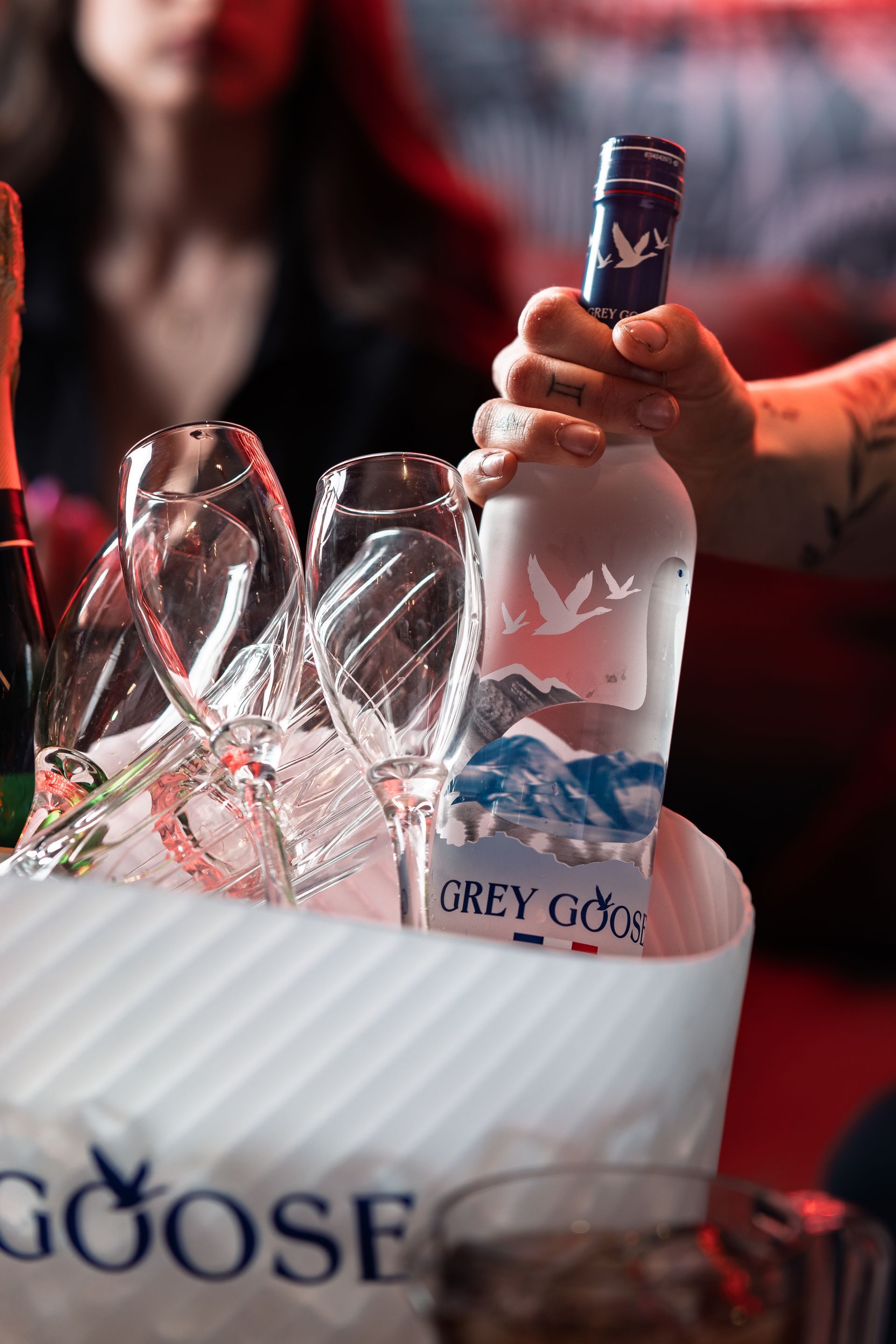 A person is pouring a bottle of grey goose vodka into a bucket of ice.