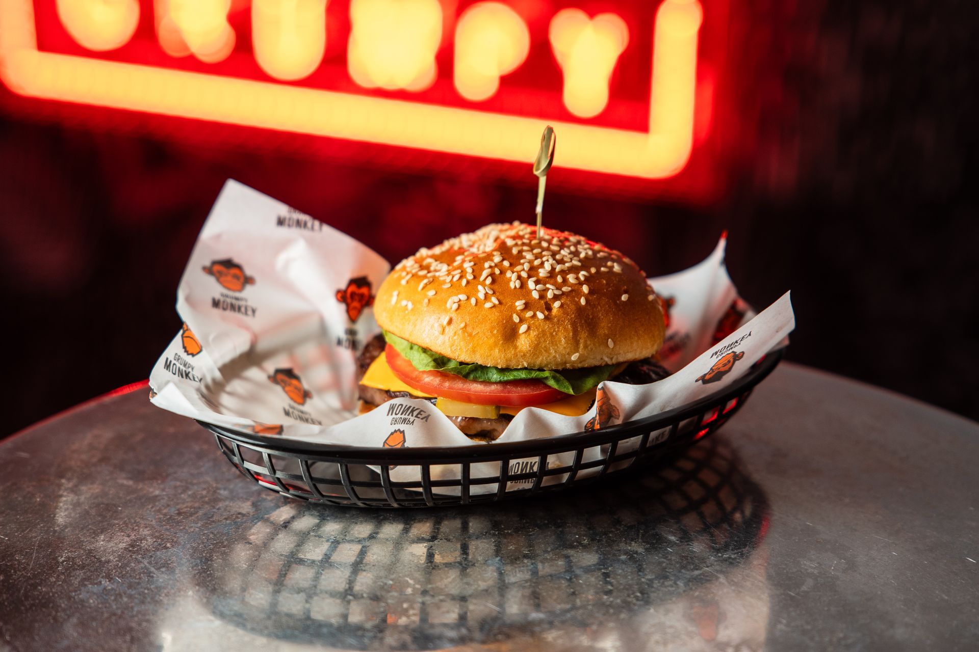 A hamburger in a basket on a table in front of a sign that says grumpy