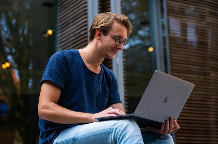 A man is sitting on a porch using a laptop computer.