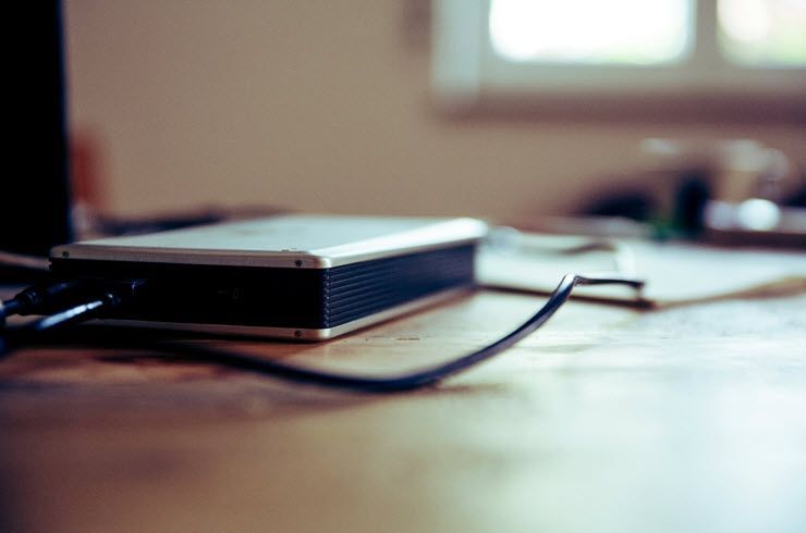 A hard drive is sitting on a wooden table next to a laptop.