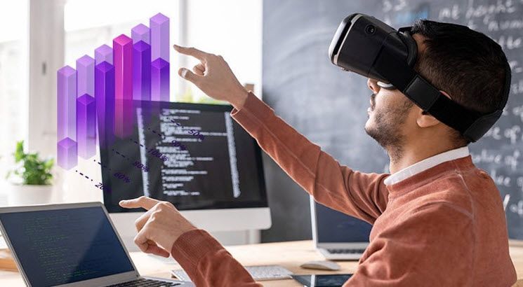 A man wearing a virtual reality headset is pointing at a computer screen.