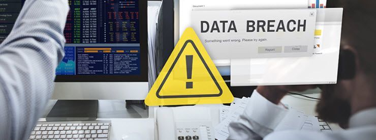 A man is sitting at a desk with a laptop and a sign that says data breach.