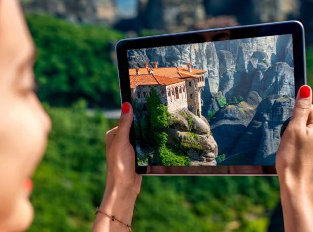 A woman is taking a picture of a castle on a tablet.