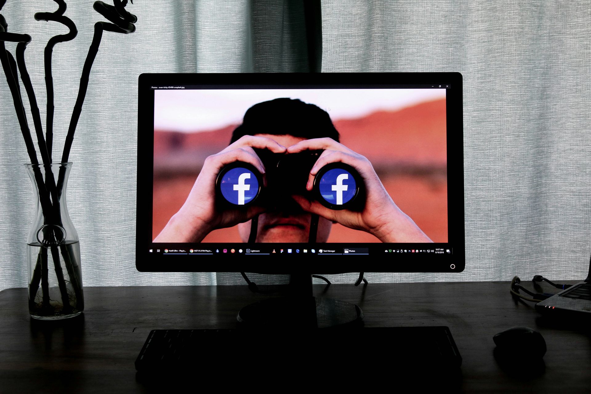 A computer monitor shows a man looking through binoculars with a facebook logo on the screen.