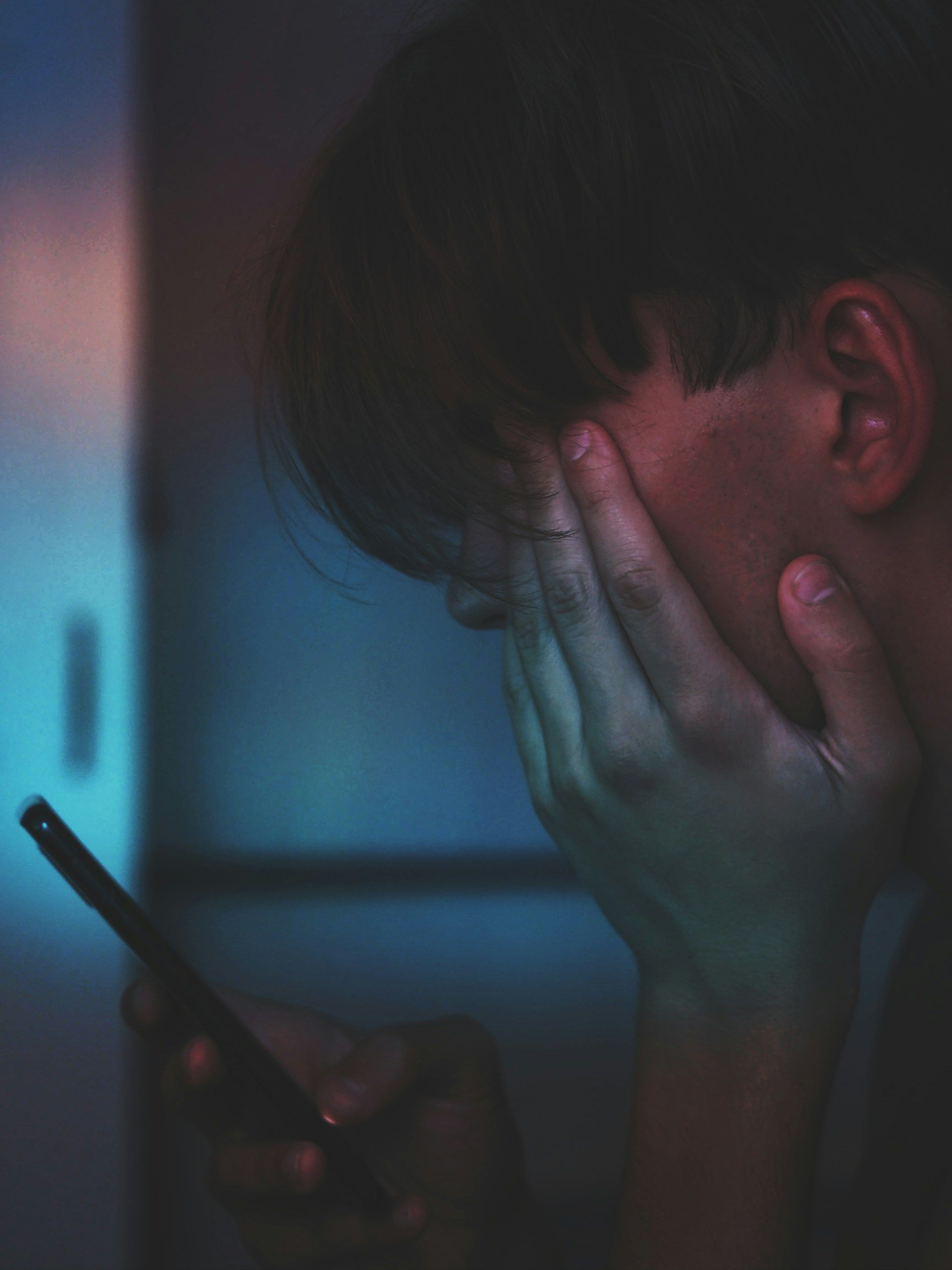 A man is covering his face while looking at a cell phone.