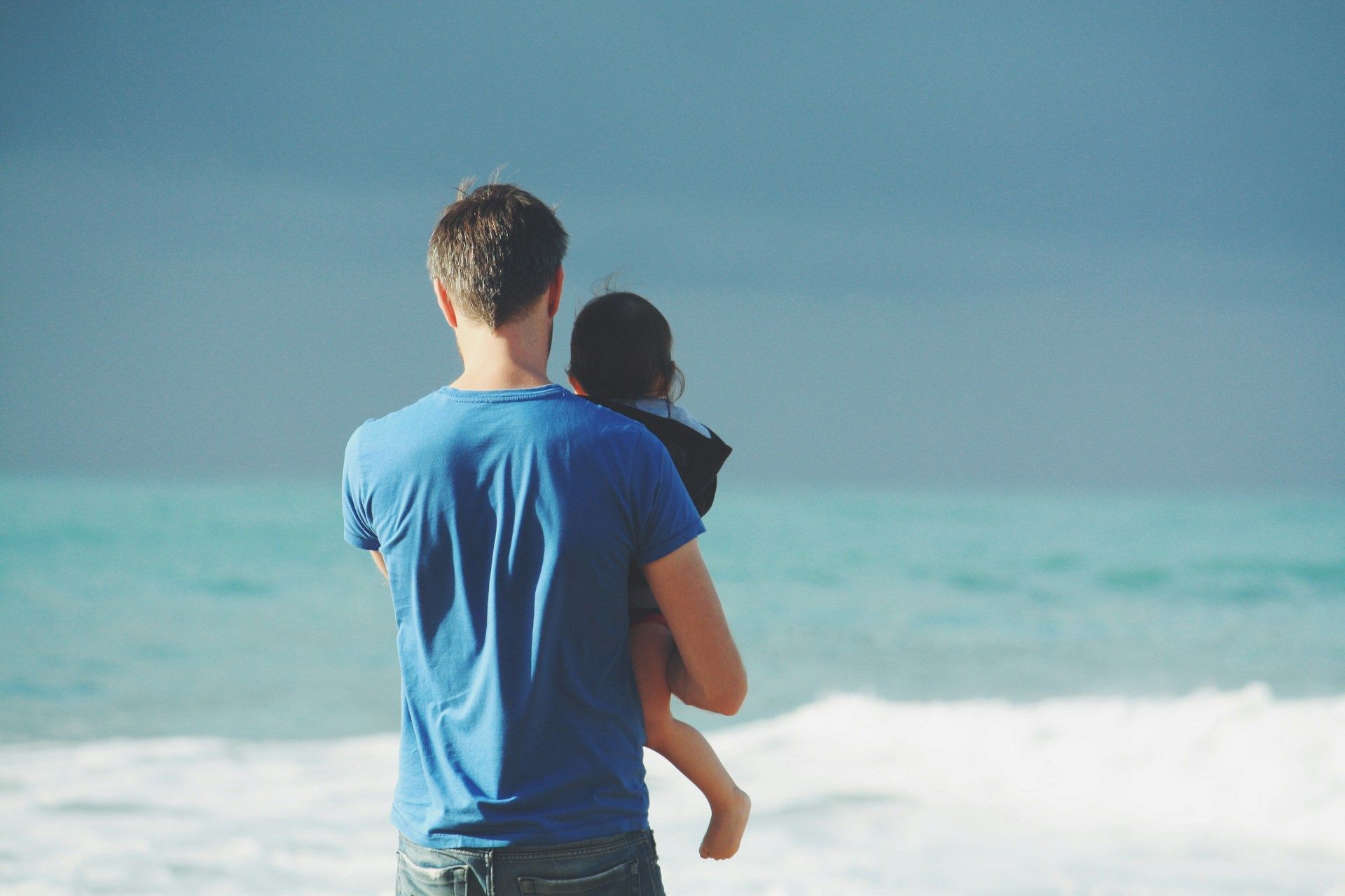 A man is holding a baby on the beach.