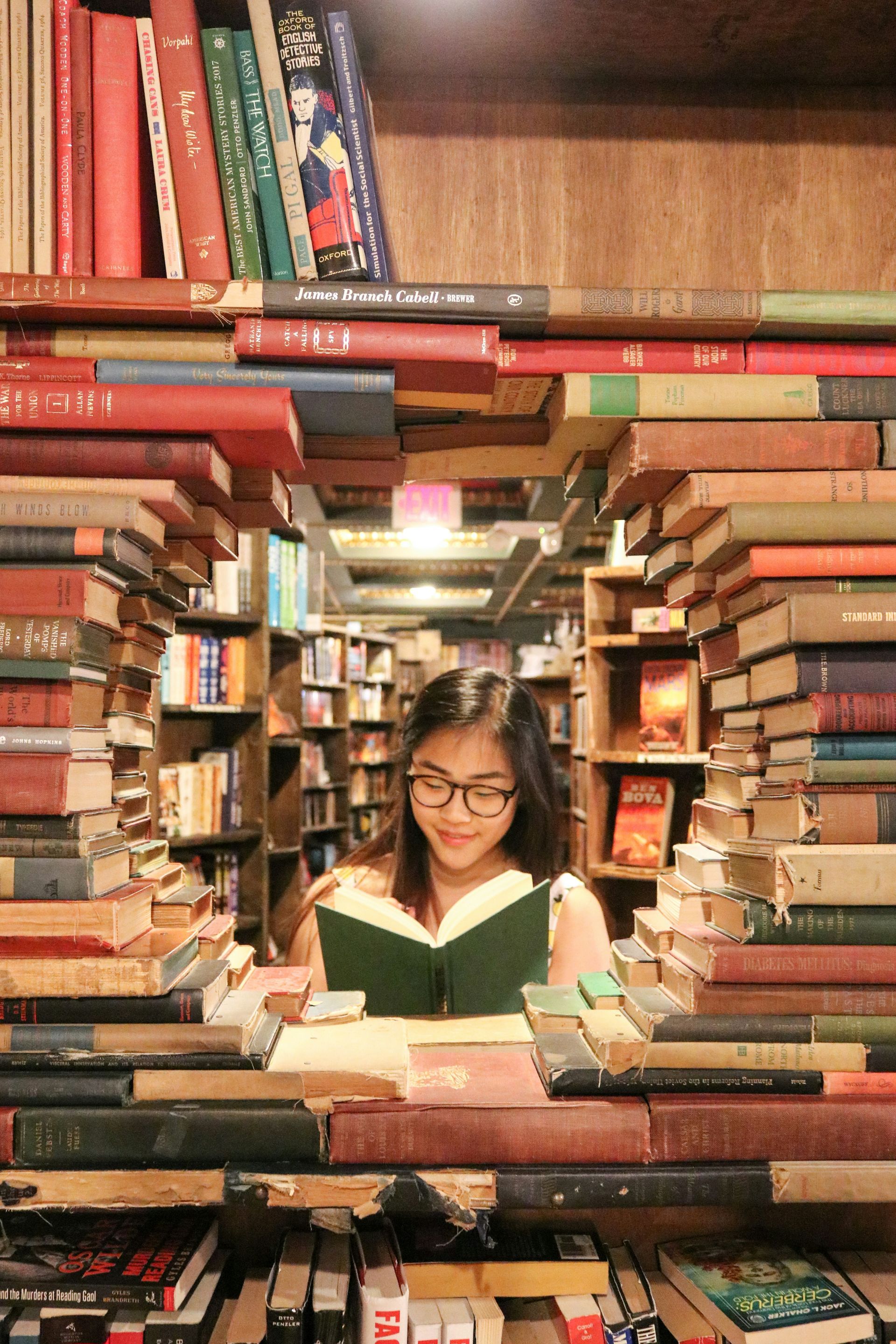 A woman is reading a book in a library surrounded by books.