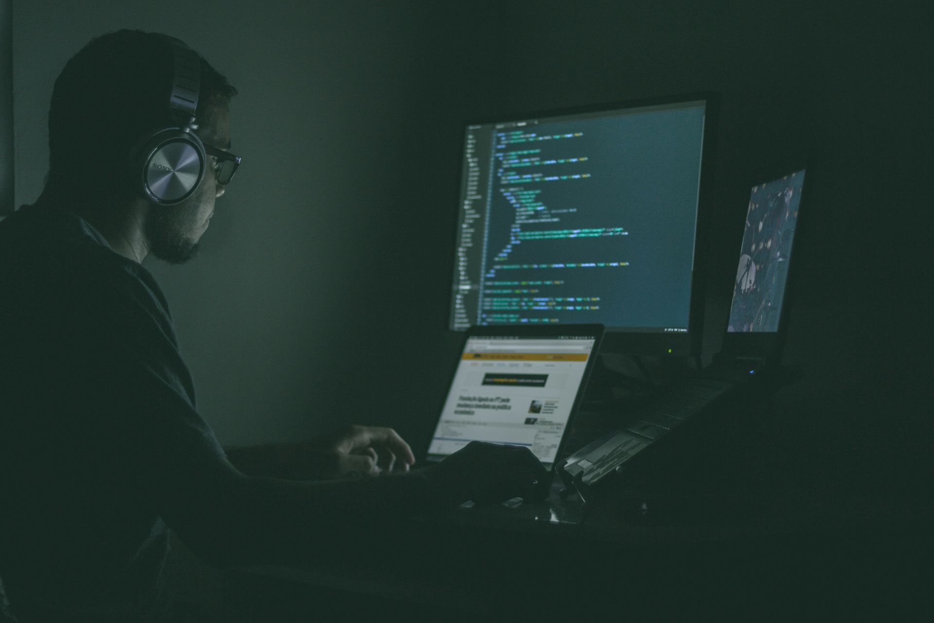 A man wearing headphones is sitting in front of a computer in a dark room.