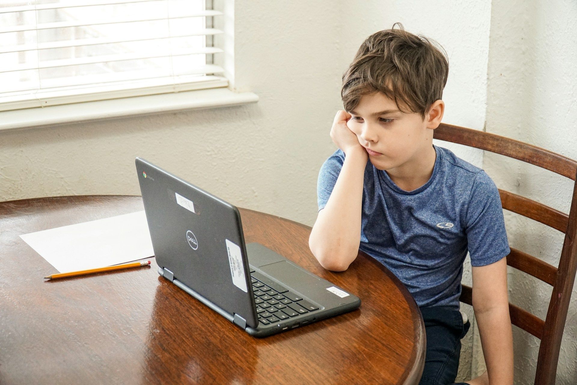 A young boy is sitting at a table using a laptop computer.