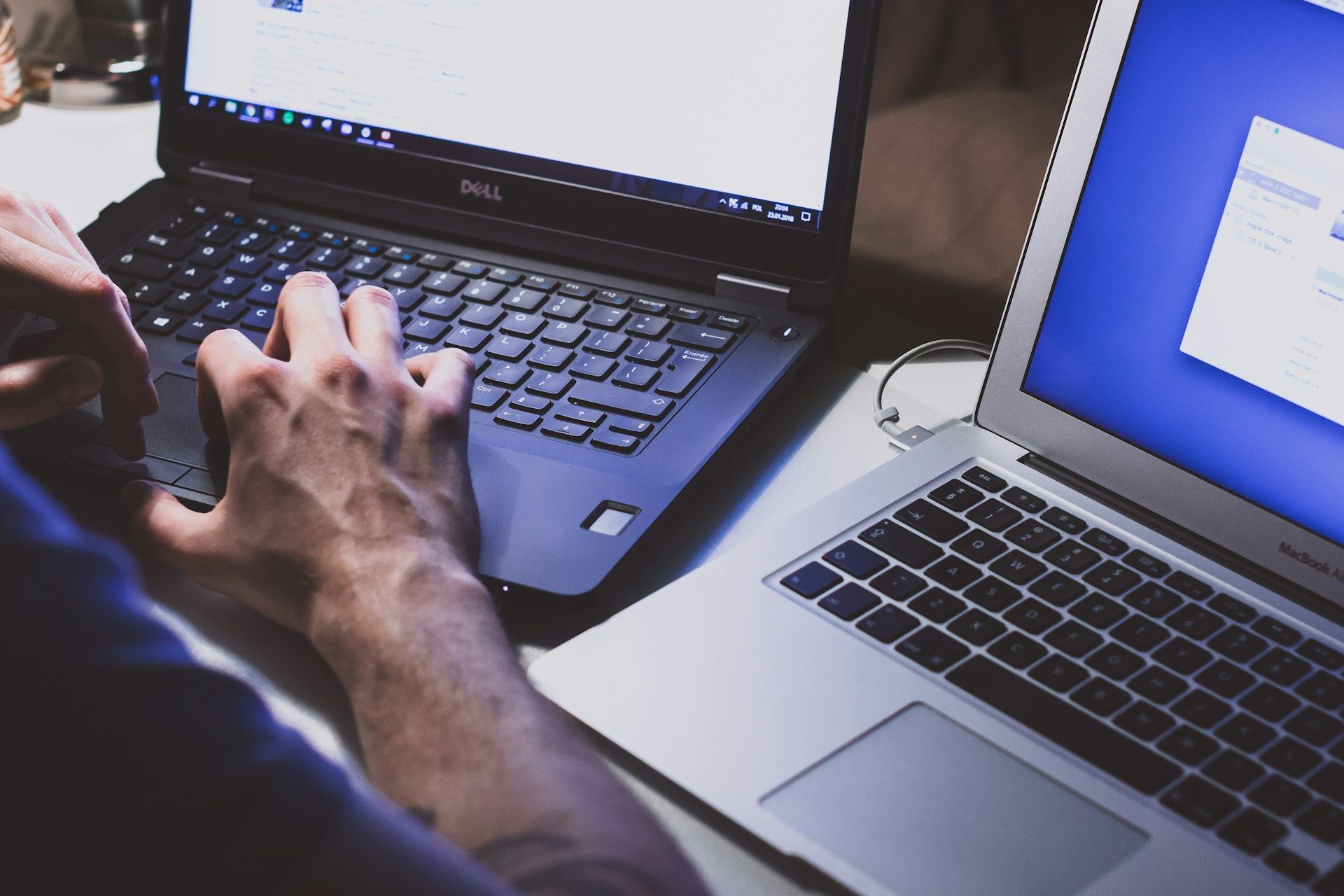 A person is typing on a dell laptop next to a macbook air laptop